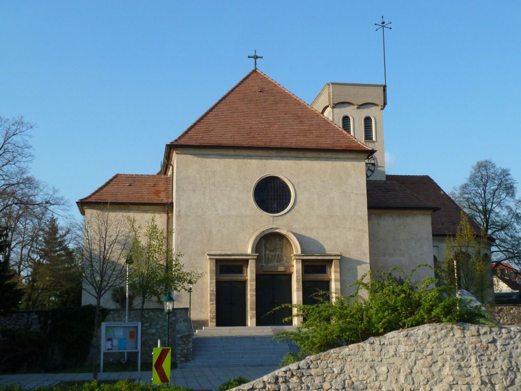 Pohľad spredu na kostol s červenou strechou a okrúhlym oknom.