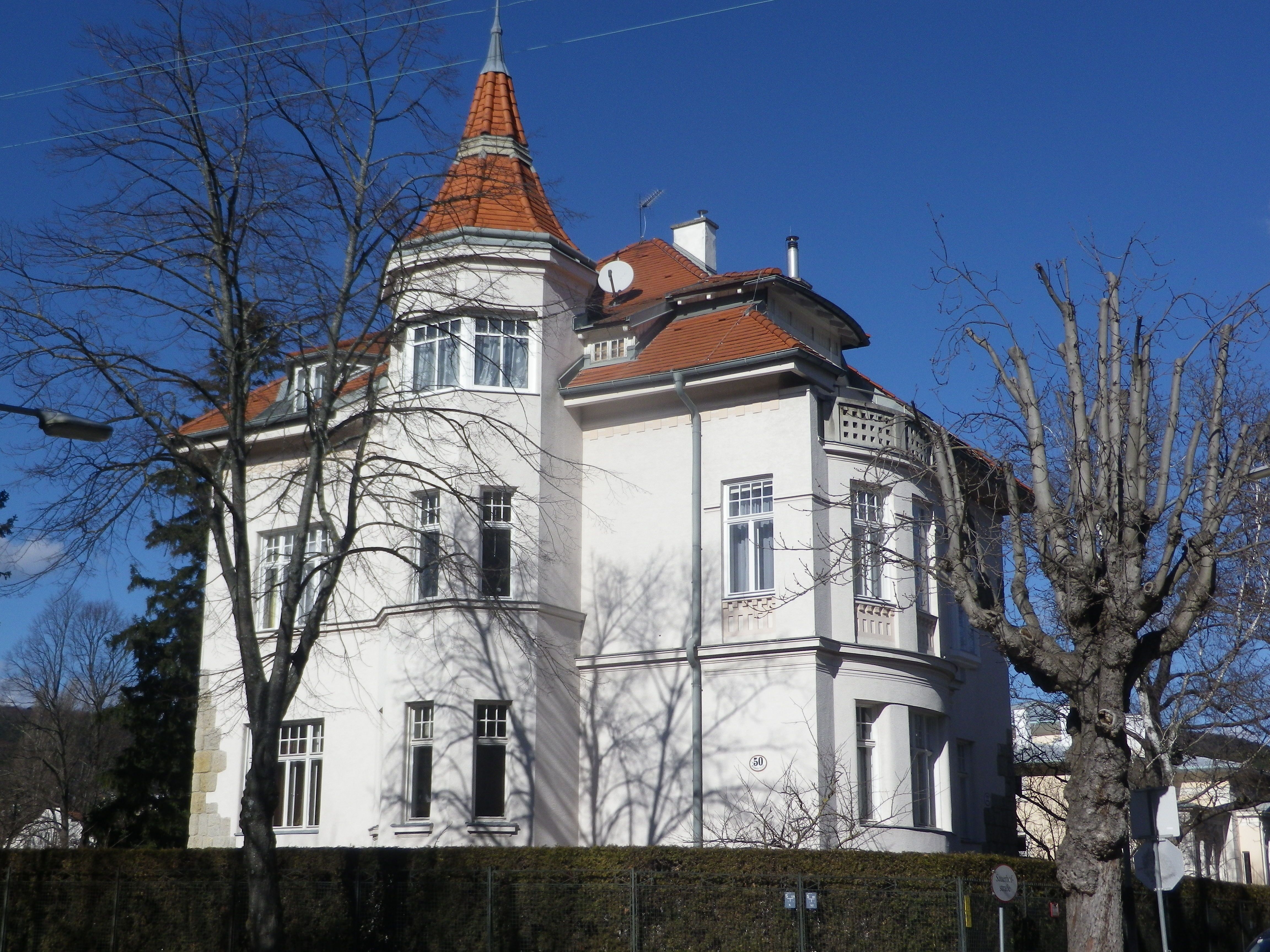 Veľký biely dom s červenou strechou a vežou, obklopený holými stromami.
