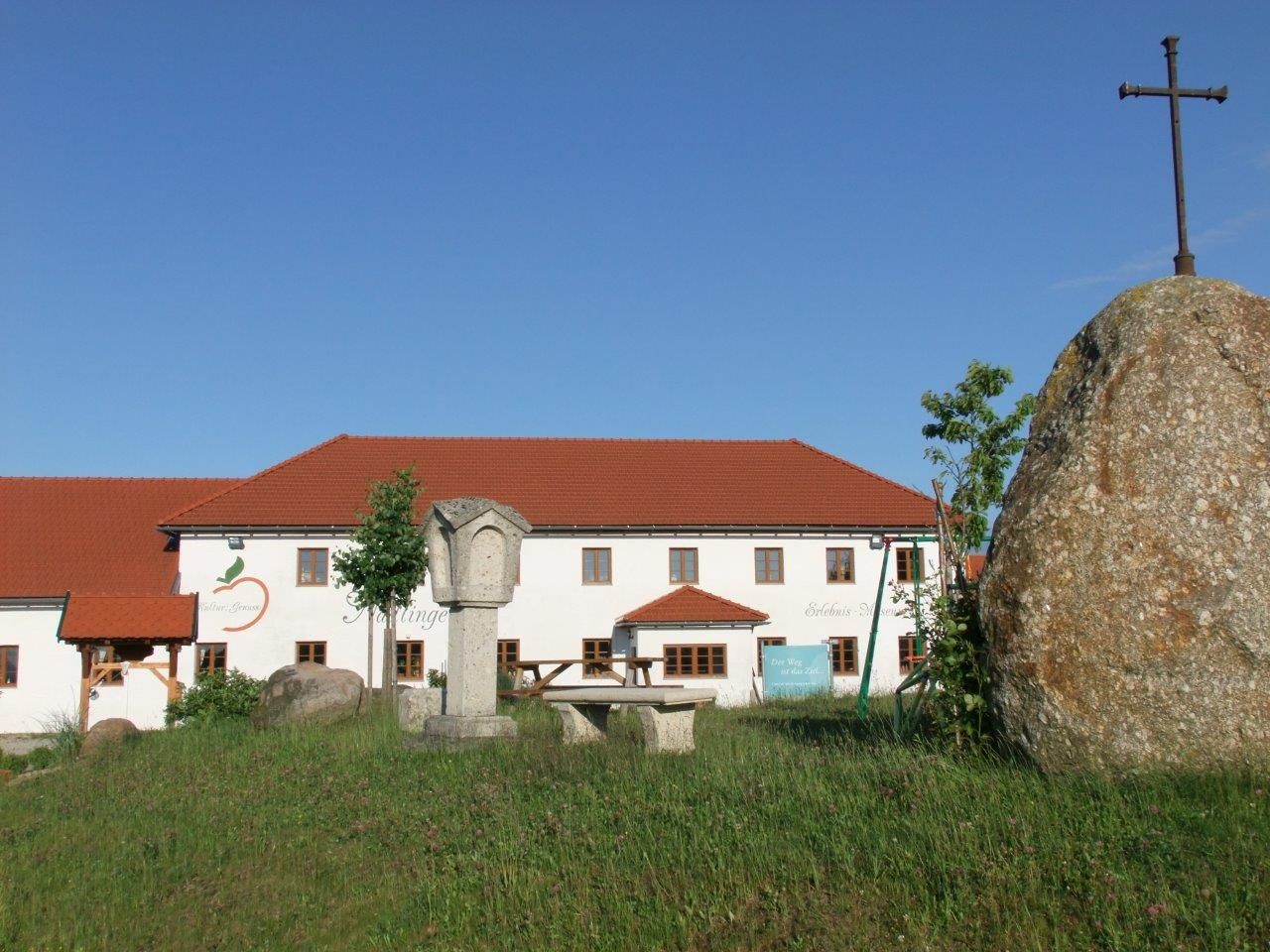Farma s červenou strechou a veľkým kameňom s krížom v popredí.