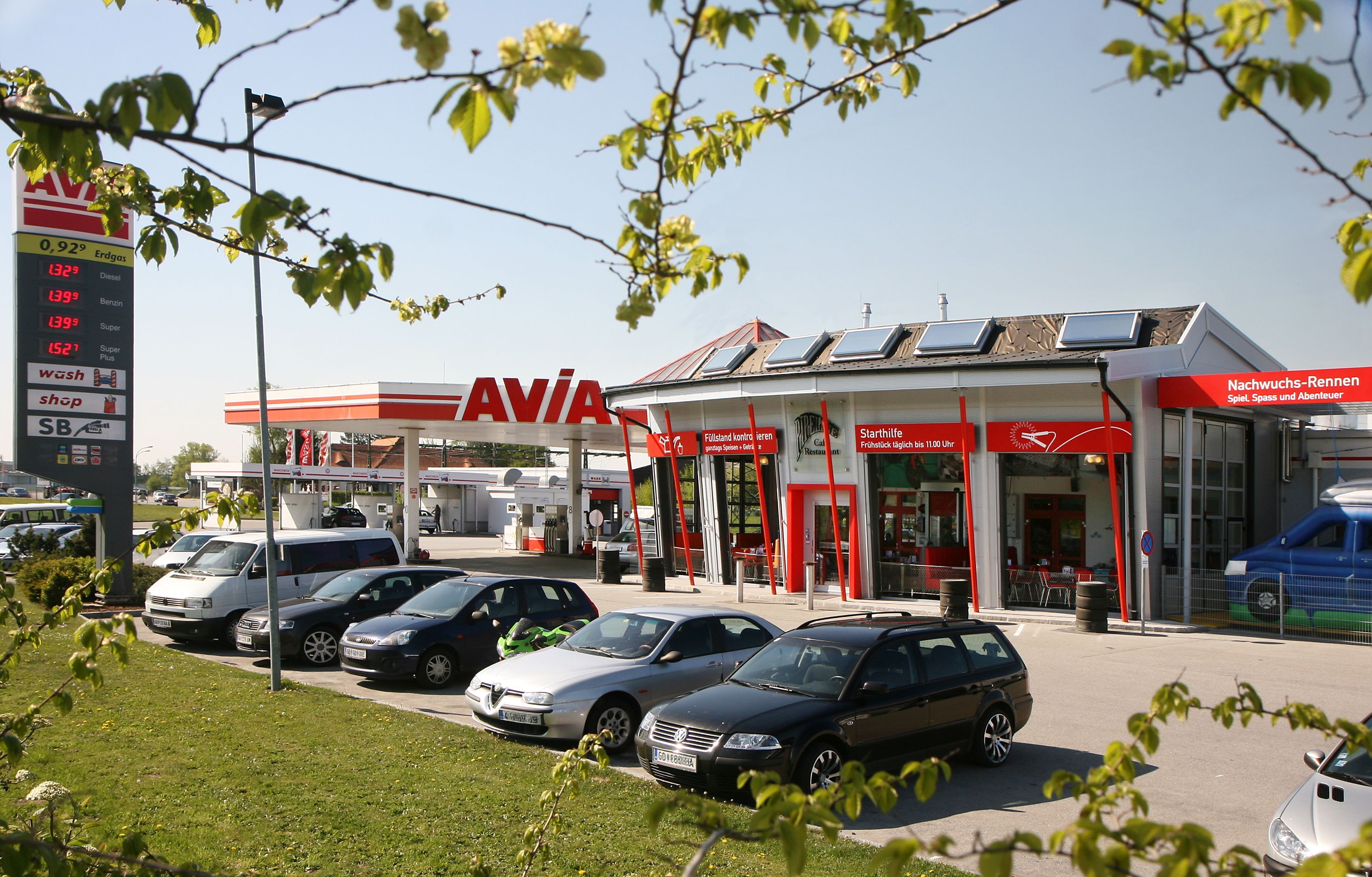 Čerpacia stanica s logom AVIA a niekoľkými zaparkovanými autami v popredí.