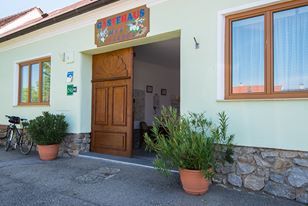 Vchod do budovy s drevenými dverami a rastlinami v kvetináčoch.