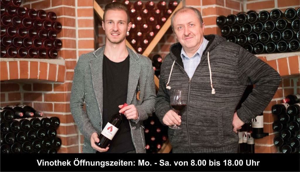 Dvaja muži vo vínnej pivnici, obklopení fľašami vína, jeden drží pohár vína.