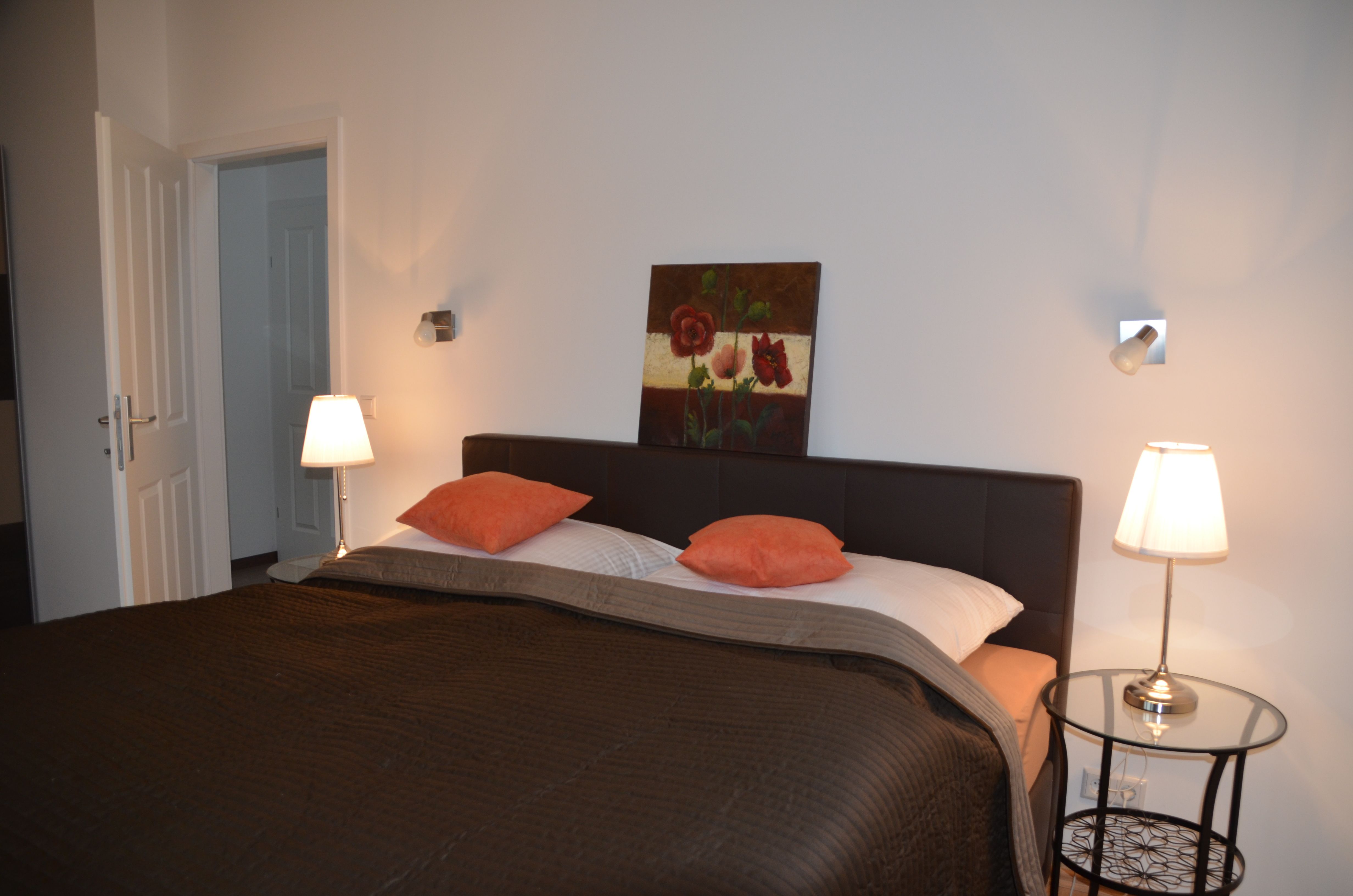 Spálňa s manželskou posteľou, dvoma nočnými lampami a obrazom na stene.