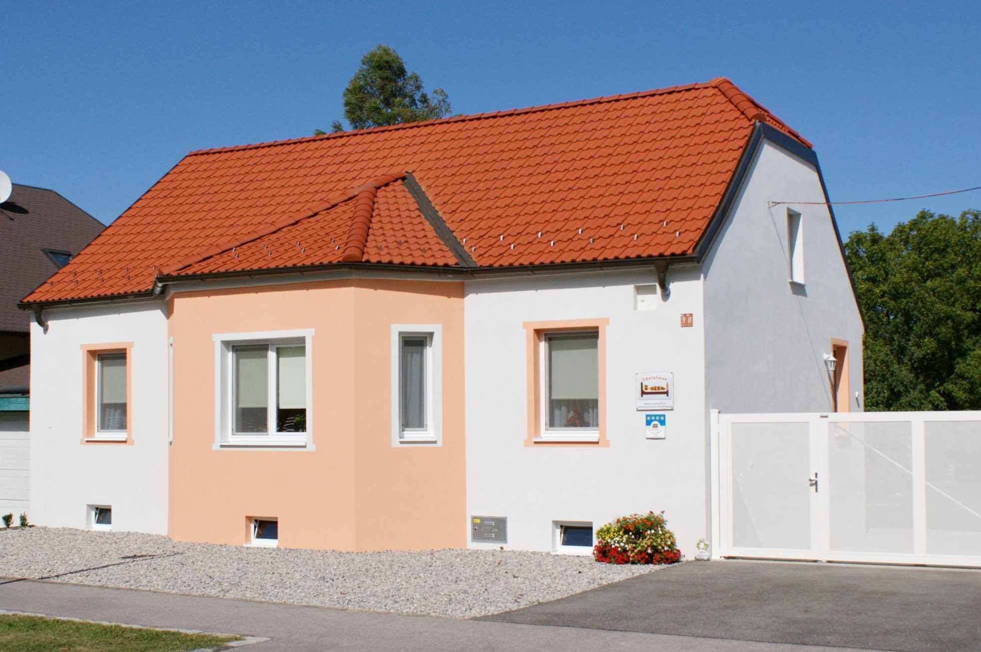 Malý jednoposchodový dom s oranžovou strechou a bielou fasádou pod modrou oblohou.