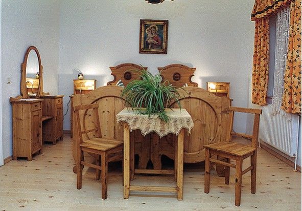 Rustikálna spálňa s dreveným nábytkom, manželskou posteľou, stolíkom s rastlinou a zrkadlom.