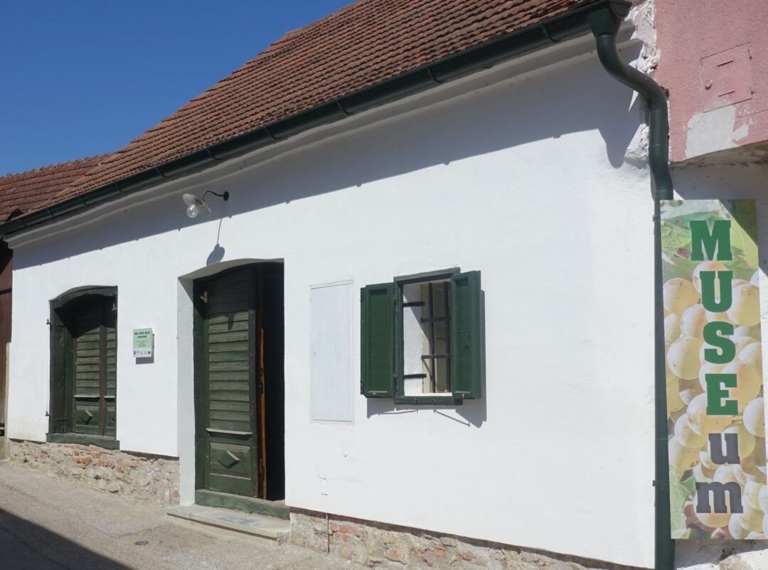 Biela budova so zelenými okenicami a dverami, nápis "MUSEUM".