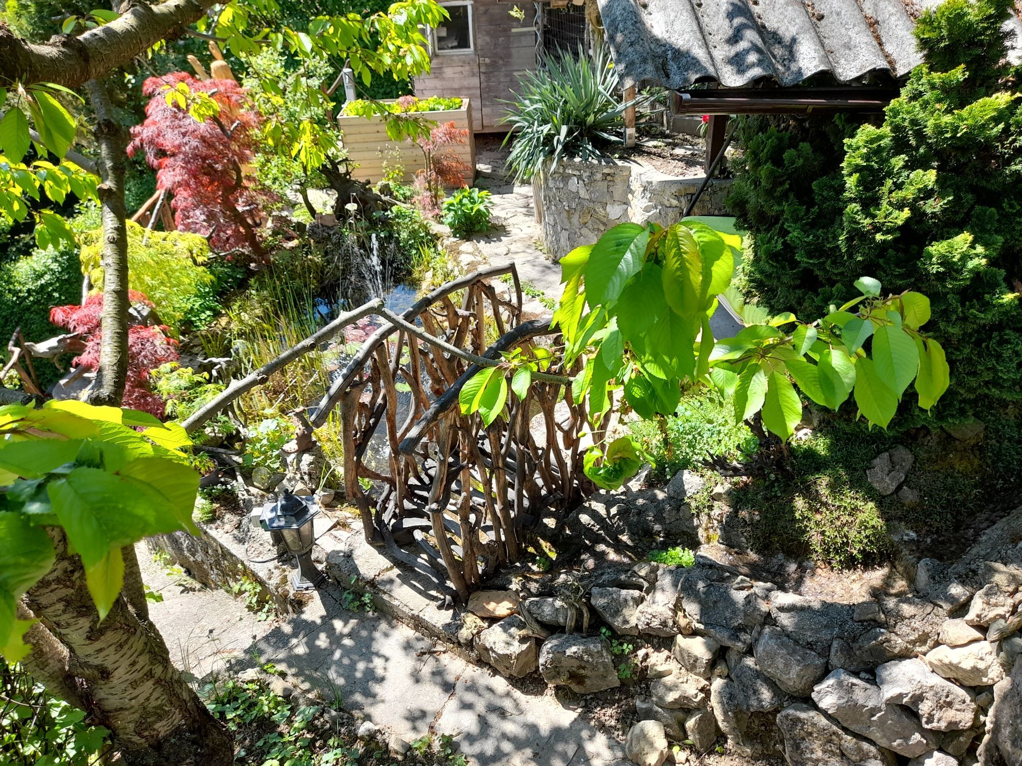 Záhrada s dreveným mostom, rastlinami a kameňmi.