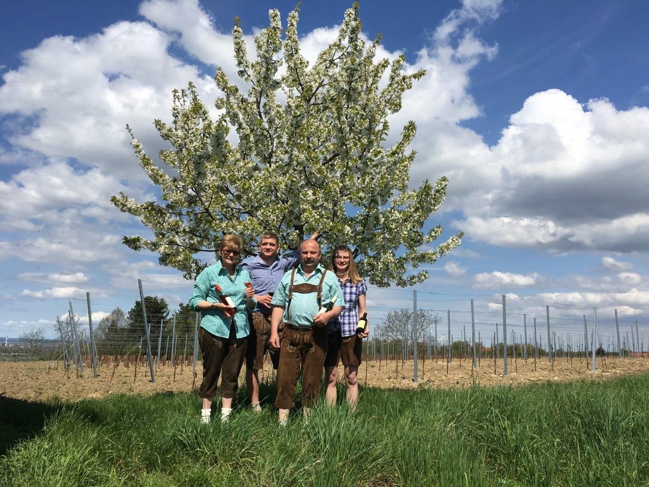Štyria ľudia stoja pred rozkvitnutým stromom na poli.