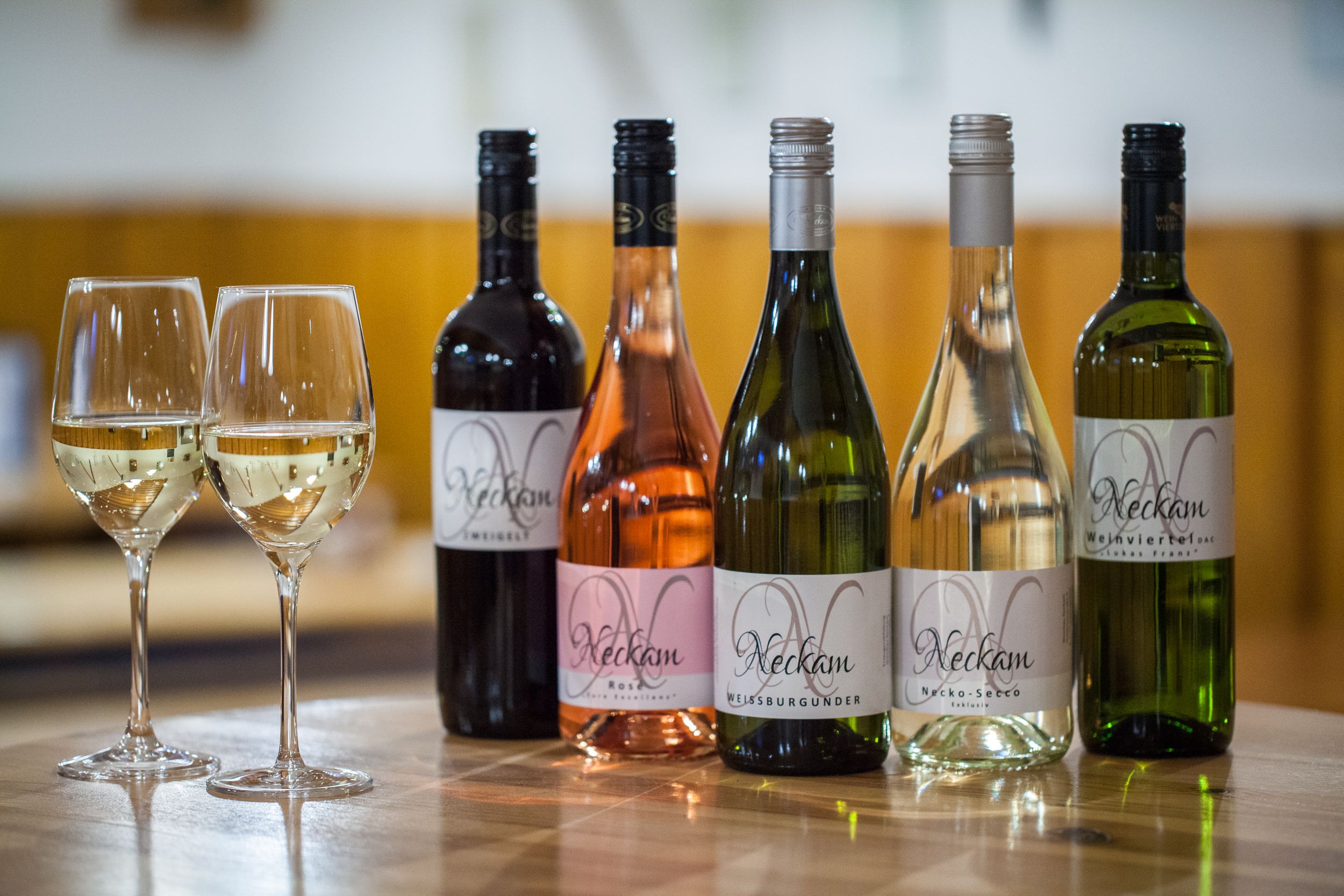 Päť fliaš vína a dva plné poháre na drevenom stole.