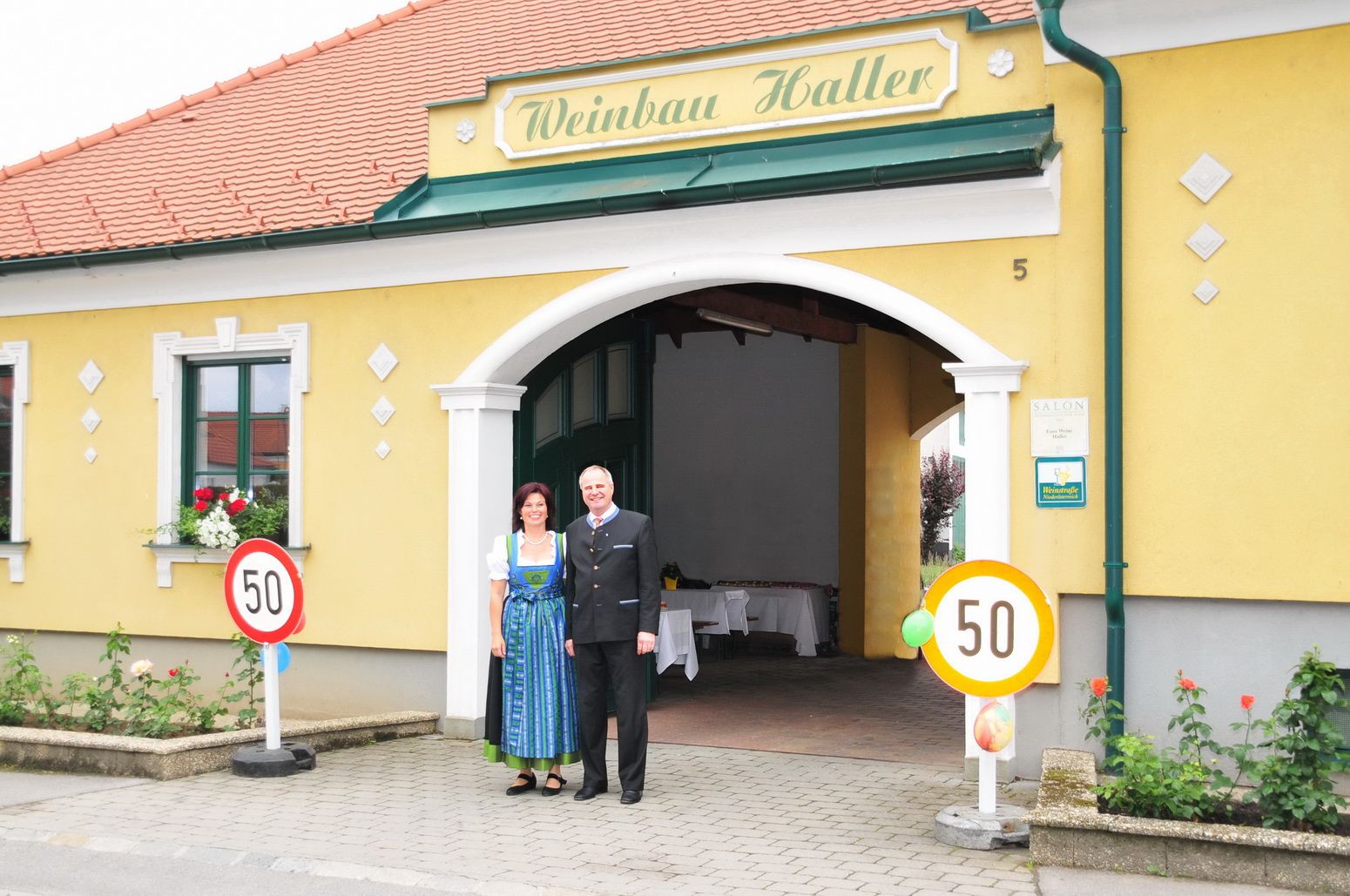 Dvojica stojí pred žltou budovou s nápisom "Weinbau Haller".