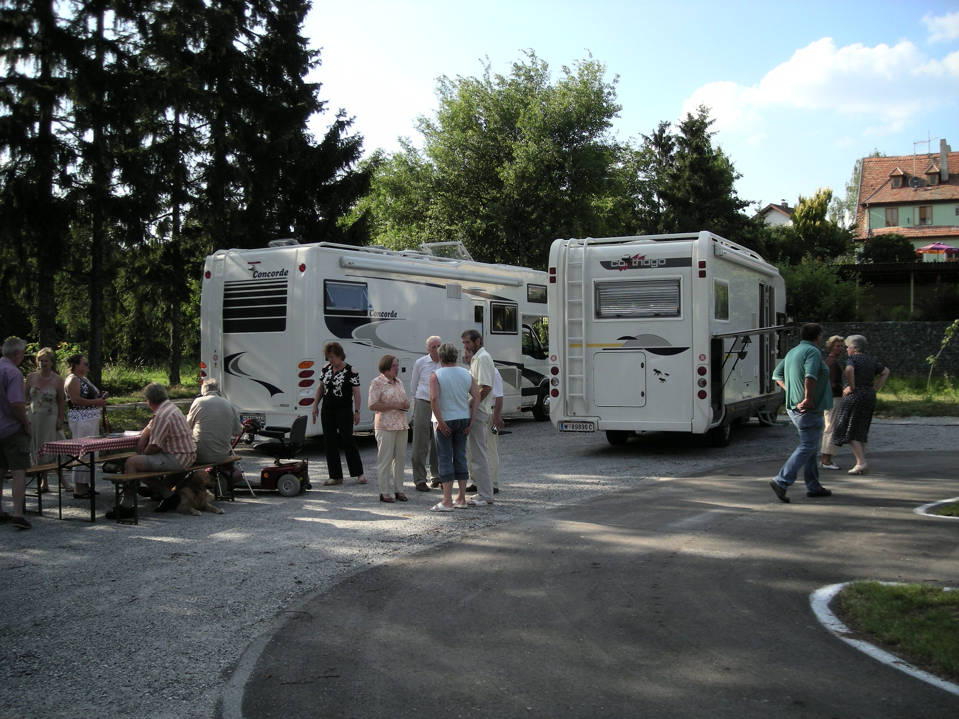 Ľudia stoja a sedia vedľa dvoch mobilných domov na vonkajšom ihrisku.