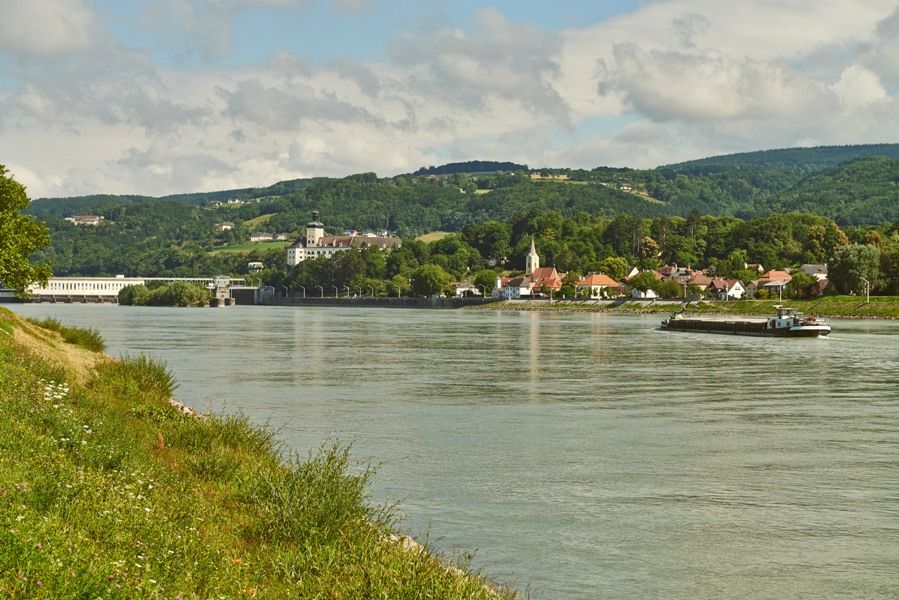 Riečna krajina s dedinou a kopcami v pozadí.