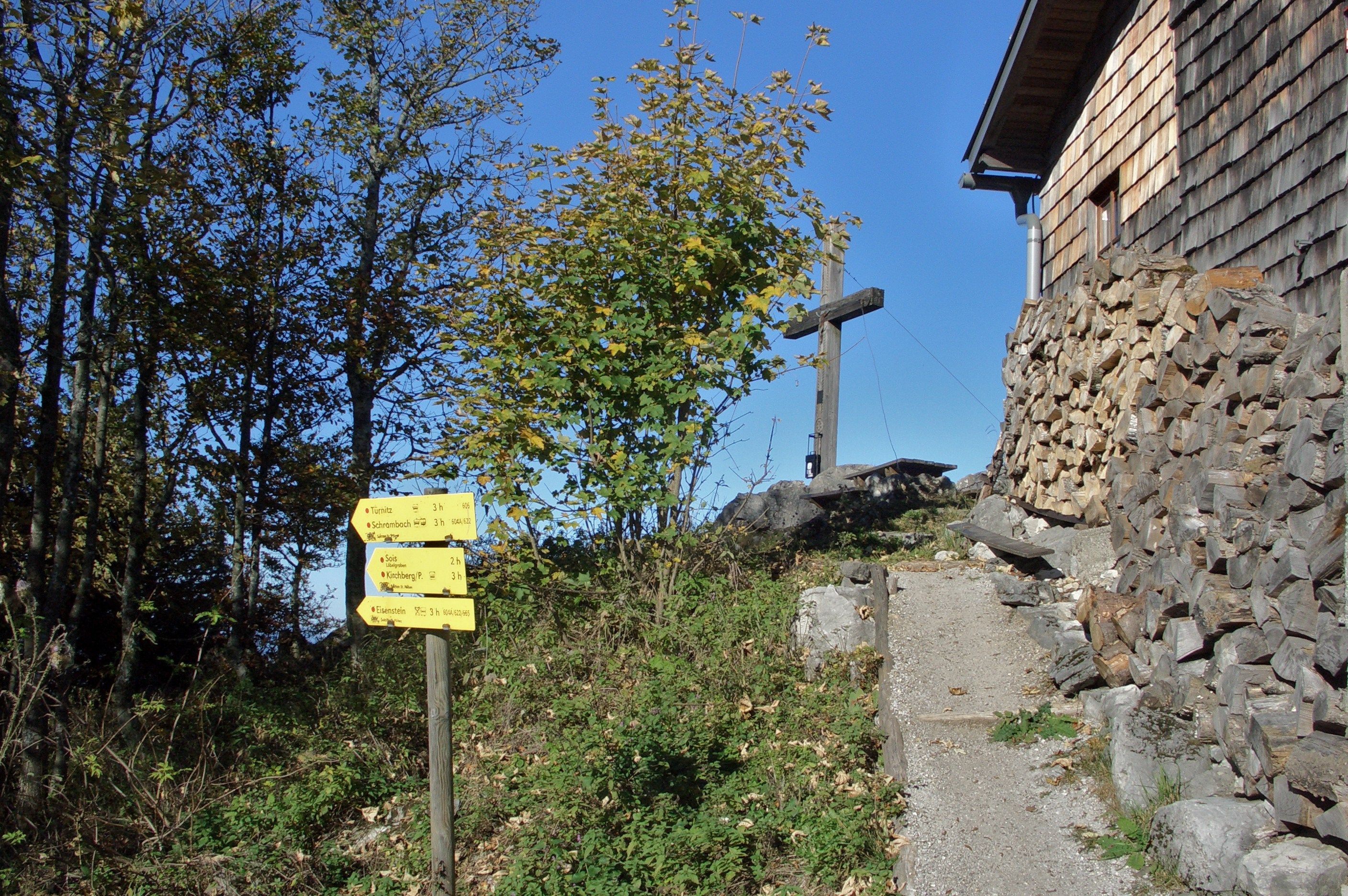 Smerovník a drevený kríž pri drevenom dome v horskej krajine.