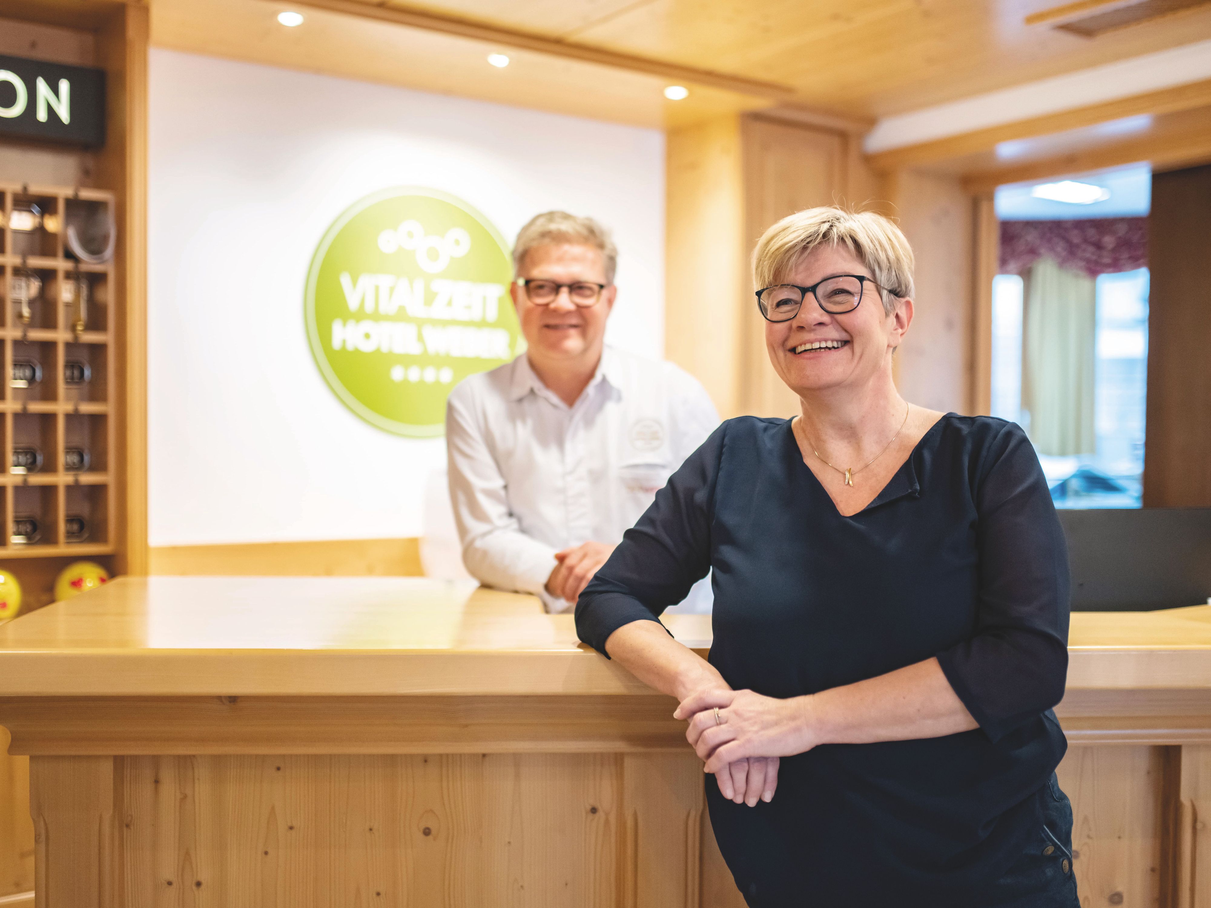 Petra a Alfred Weber stoja s úsmevom na tvári pri recepcii hotela VitalZeit Hotel Weber.