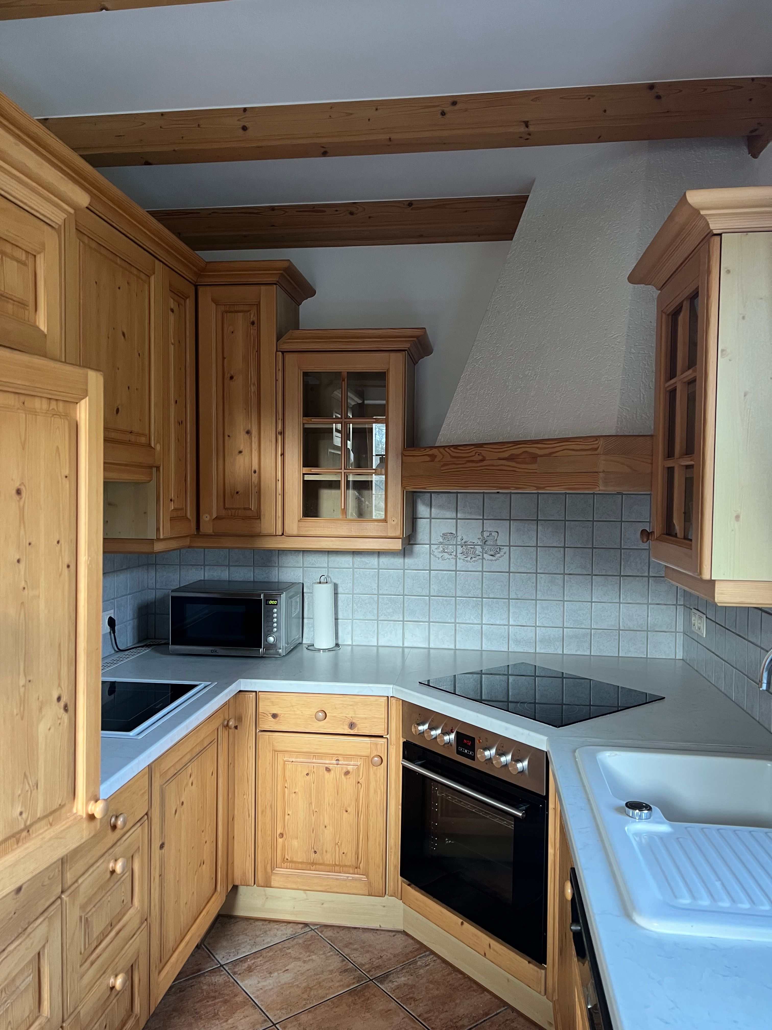 Rustikálna kuchyňa s drevenými skrinkami, elektrickým sporákom, mikrovlnnou rúrou a drezom. Steny sú obložené dlaždicami.