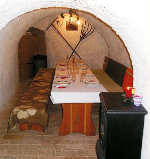 Útulná vínna pivnica s prestretým stolom a rustikálnym nábytkom.