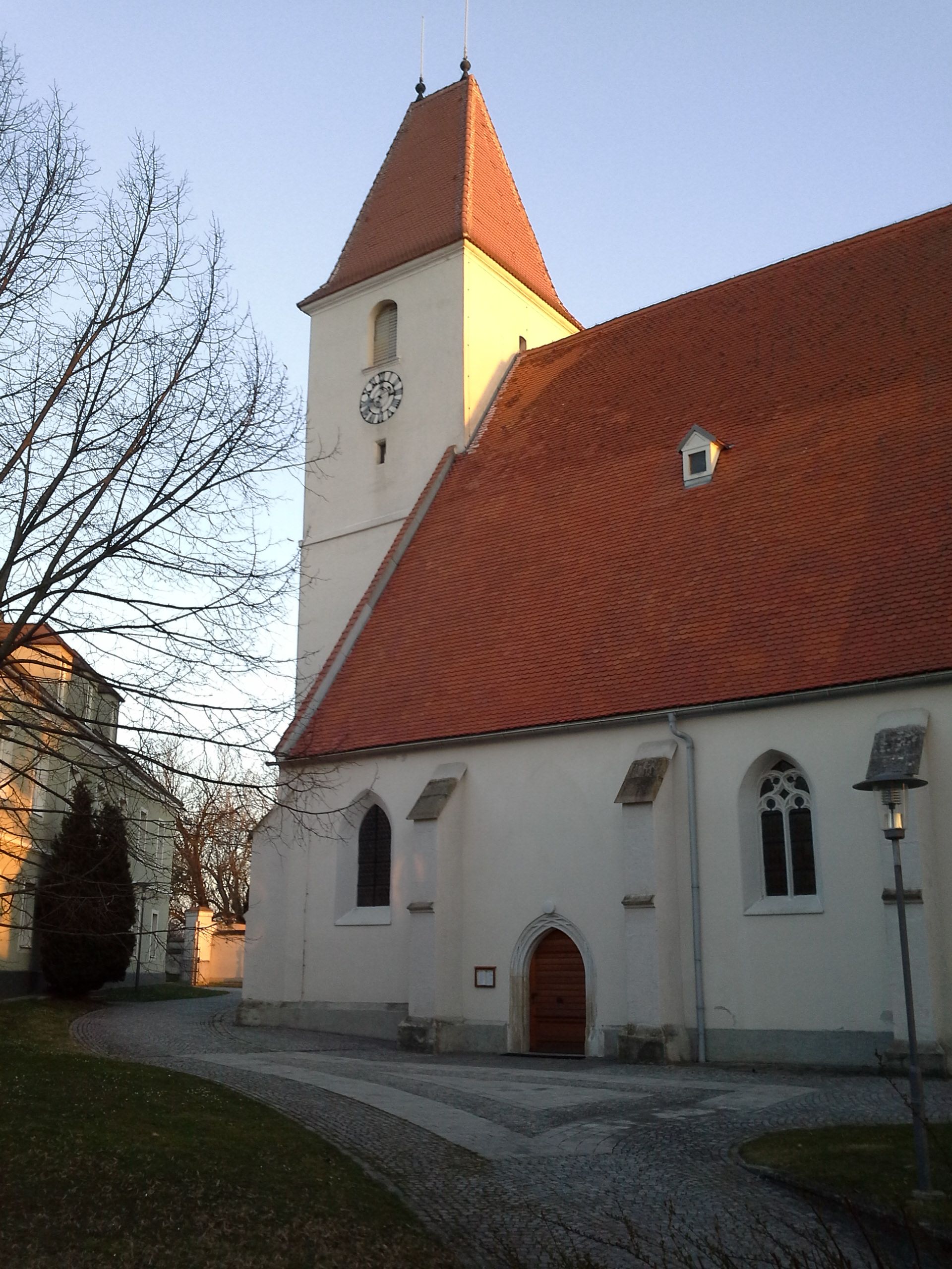 Kostol s červenou strechou a hodinovou vežou v Kapellne pri západe slnka.