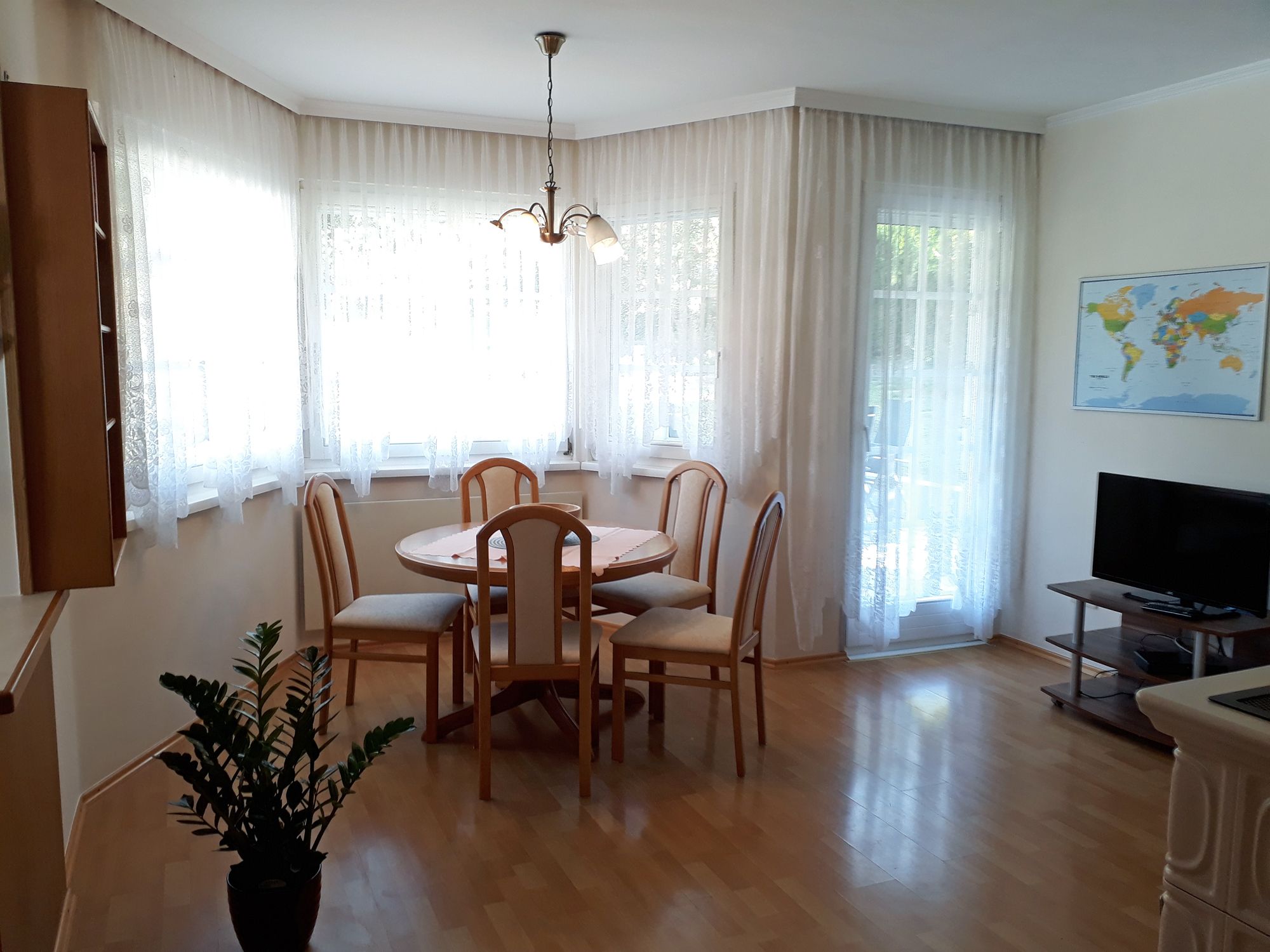 Svetlá kuchyňa s jedálenským stolom, stoličkami, TV a mapou sveta na stene.