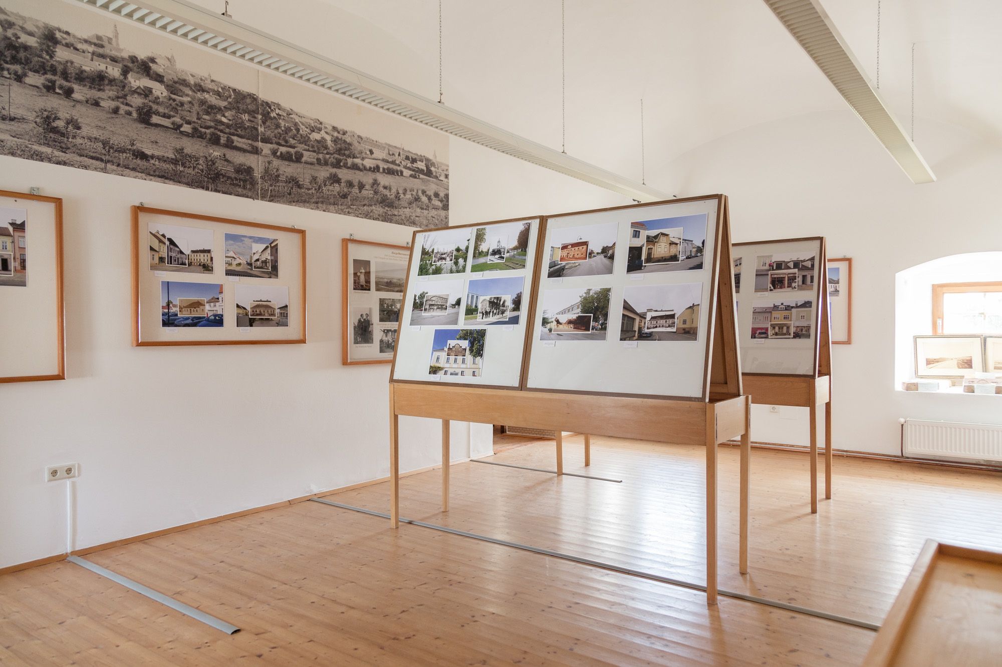 Pohľad do interiéru múzejnej miestnosti s fotografickými panelmi a historickými obrázkami na stenách.