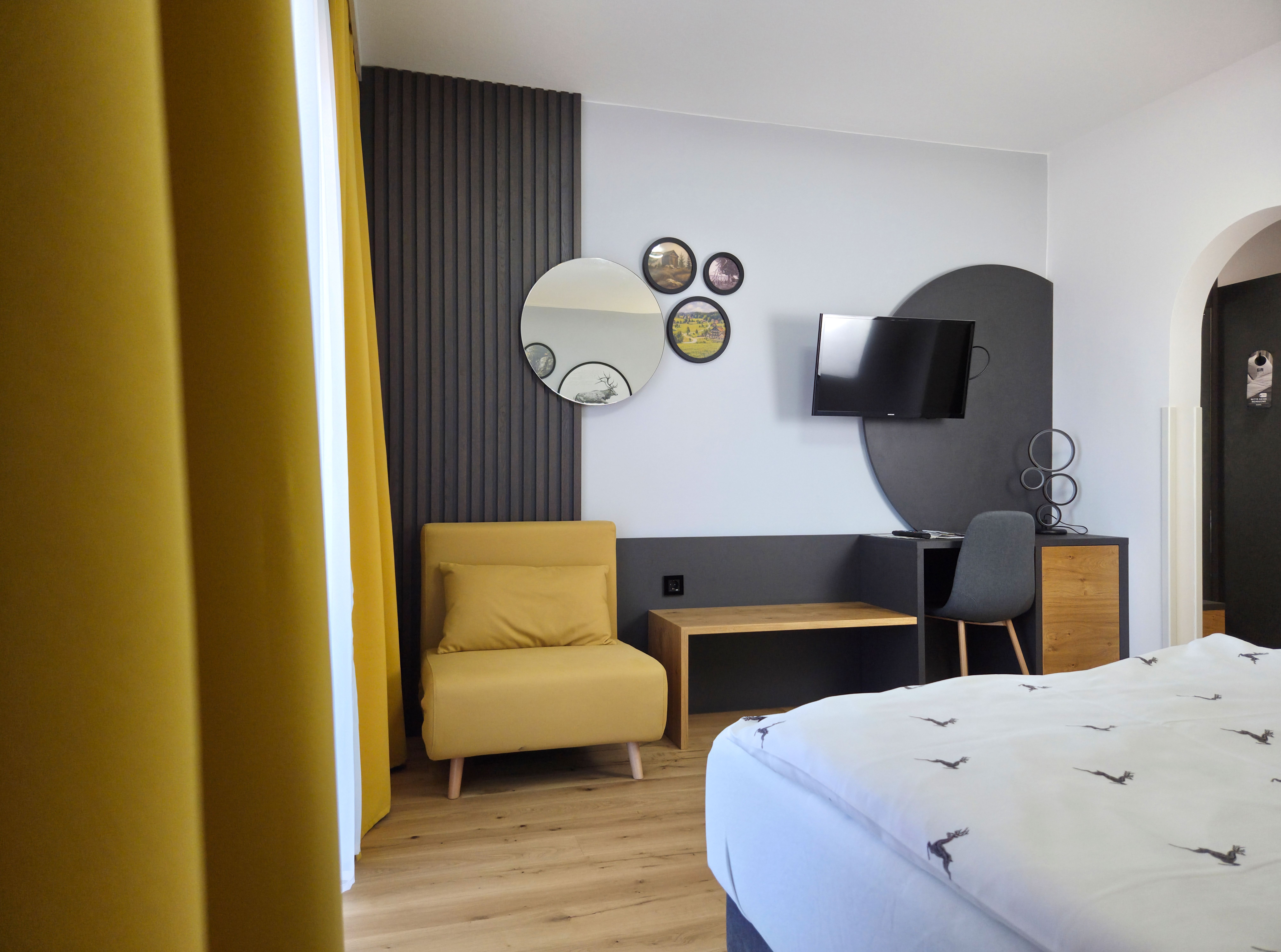 Moderne zariadená izba so žltým kreslom, zrkadlami na stene, televízorom a písacím stolom so stoličkou.