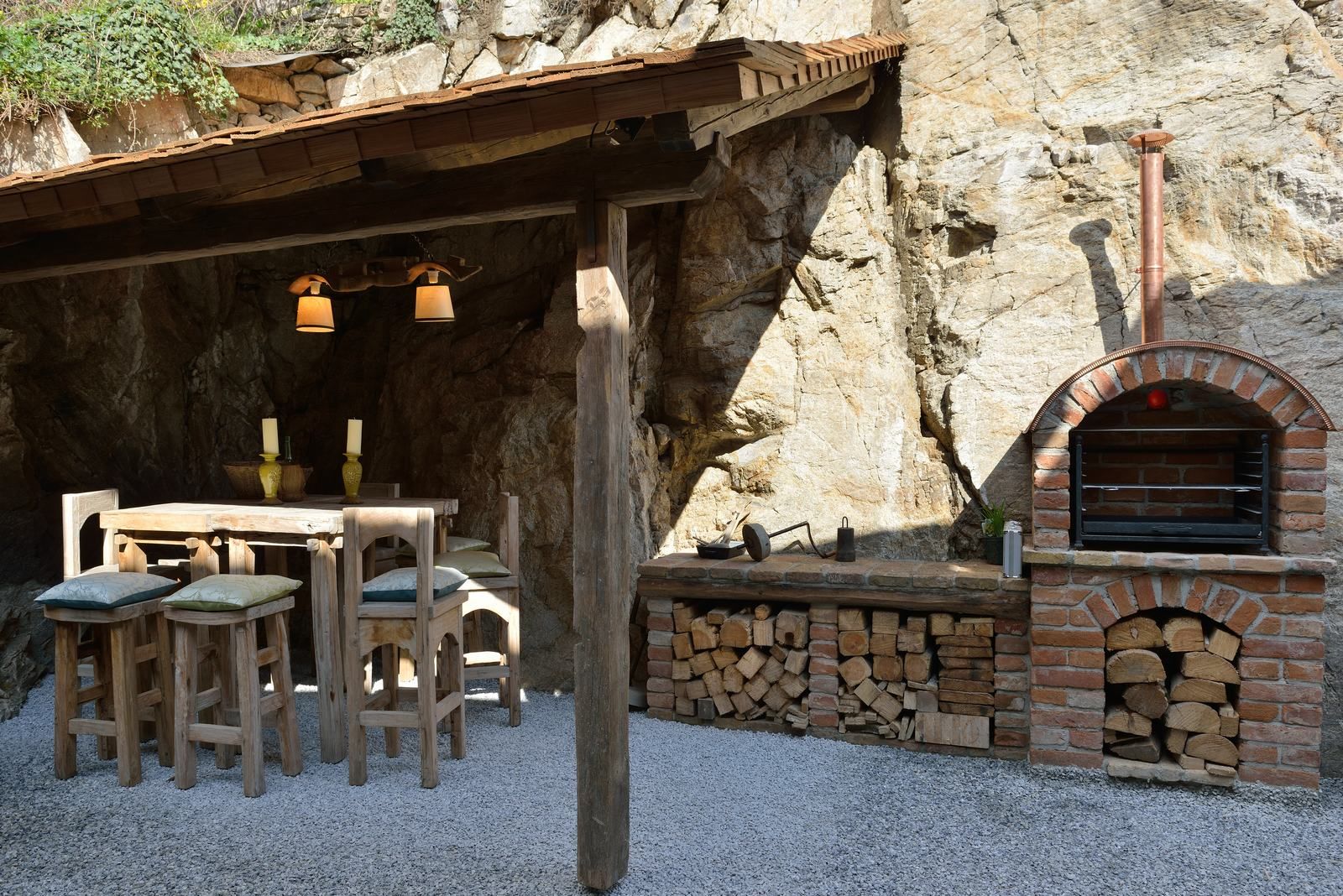 Rustikálny vonkajší priestor s dreveným stolom, stoličkami a murovanou pecou.