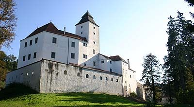 Hrad Seisenegg s bielou fasádou a vežou, obklopený stromami.
