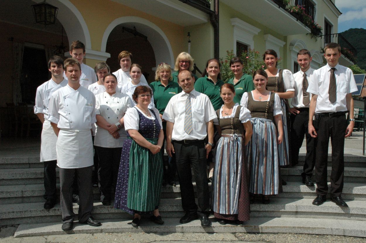 Skupina ľudí v tradičnom a profesionálnom oblečení pred budovou.