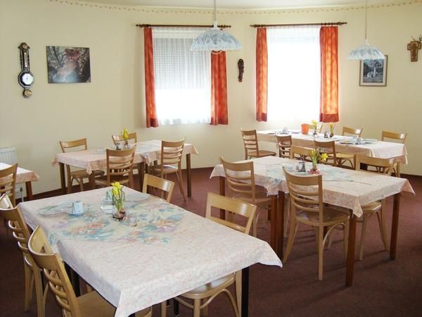 Útulná raňajková miestnosť s niekoľkými prestretými stolmi a drevenými stoličkami, vyzdobená kvetmi a obrazmi na stenách.