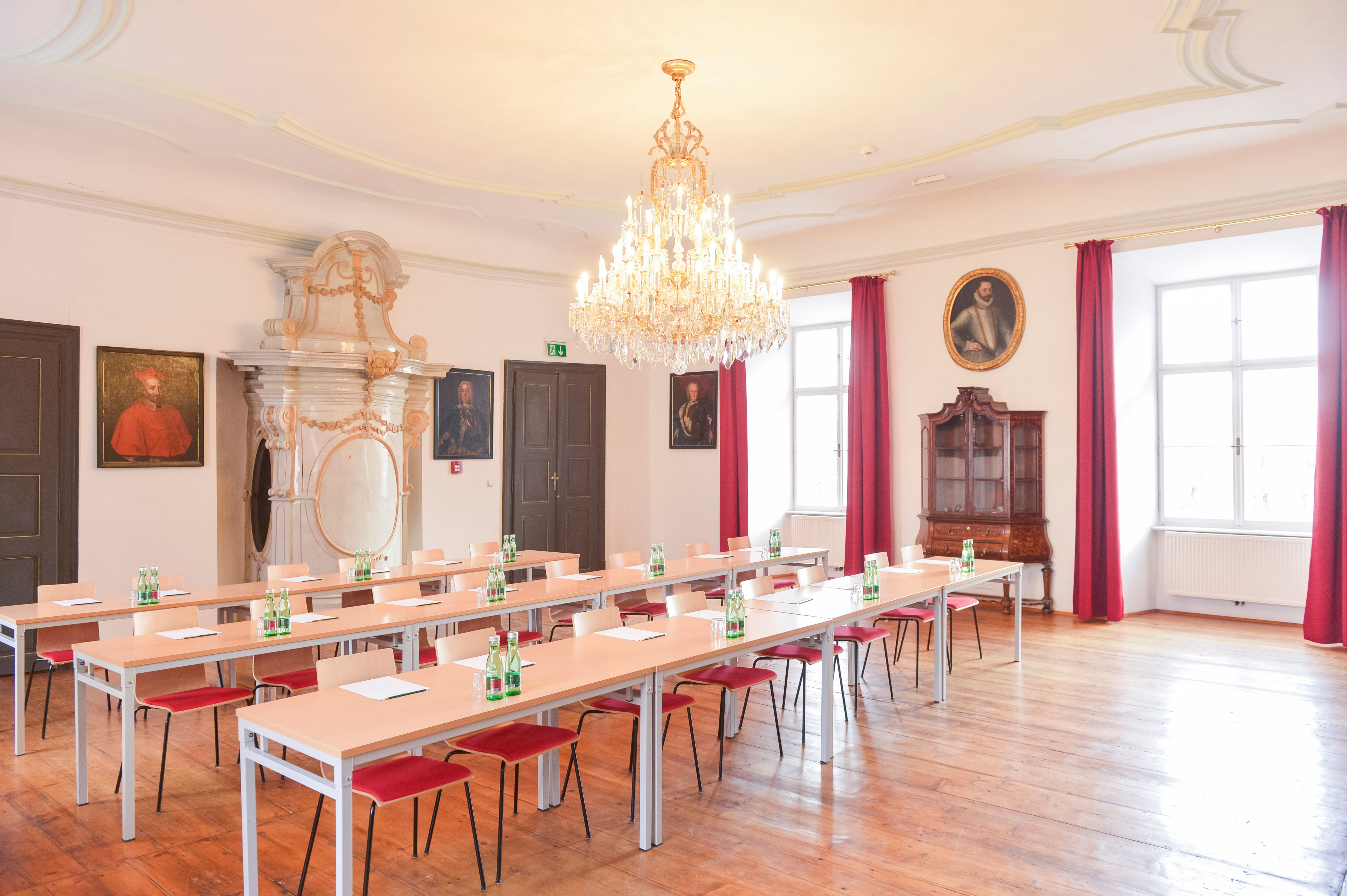 Elegantná seminárna miestnosť s lustrom, drevenou podlahou a portrétmi na stenách.