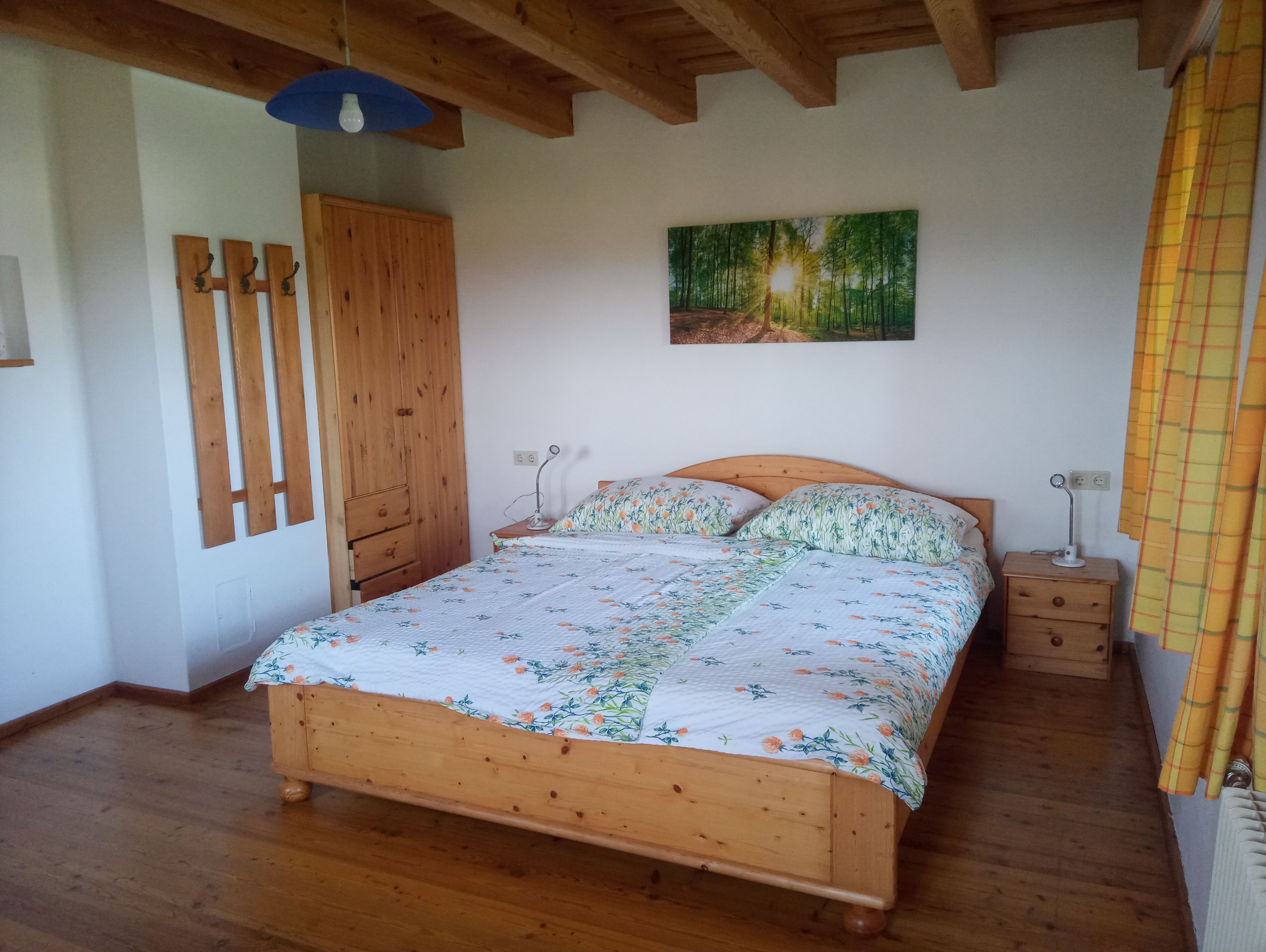 Spálňa s drevenou posteľou, nočnými stolíkmi, šatníkovou skriňou a nástennou maľbou lesa.