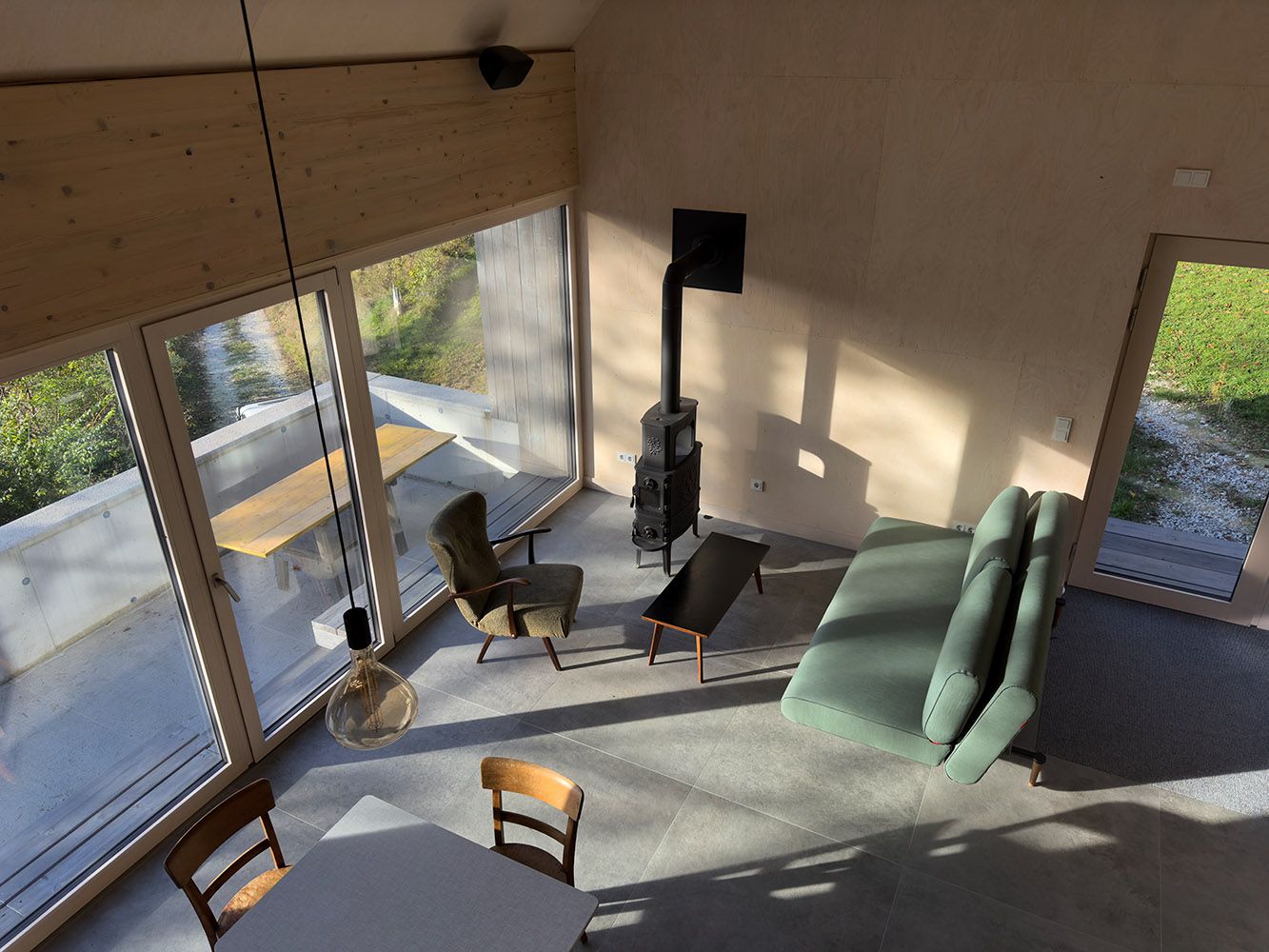 Moderný obývací a jedálenský priestor s veľkými oknami, pohovkou, kreslom a krbom.