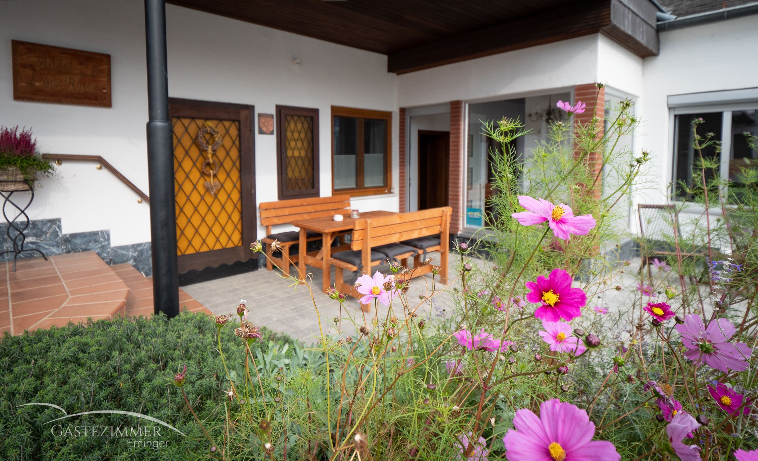 Terasa s dreveným nábytkom a rozkvitnutými kvetmi v popredí.