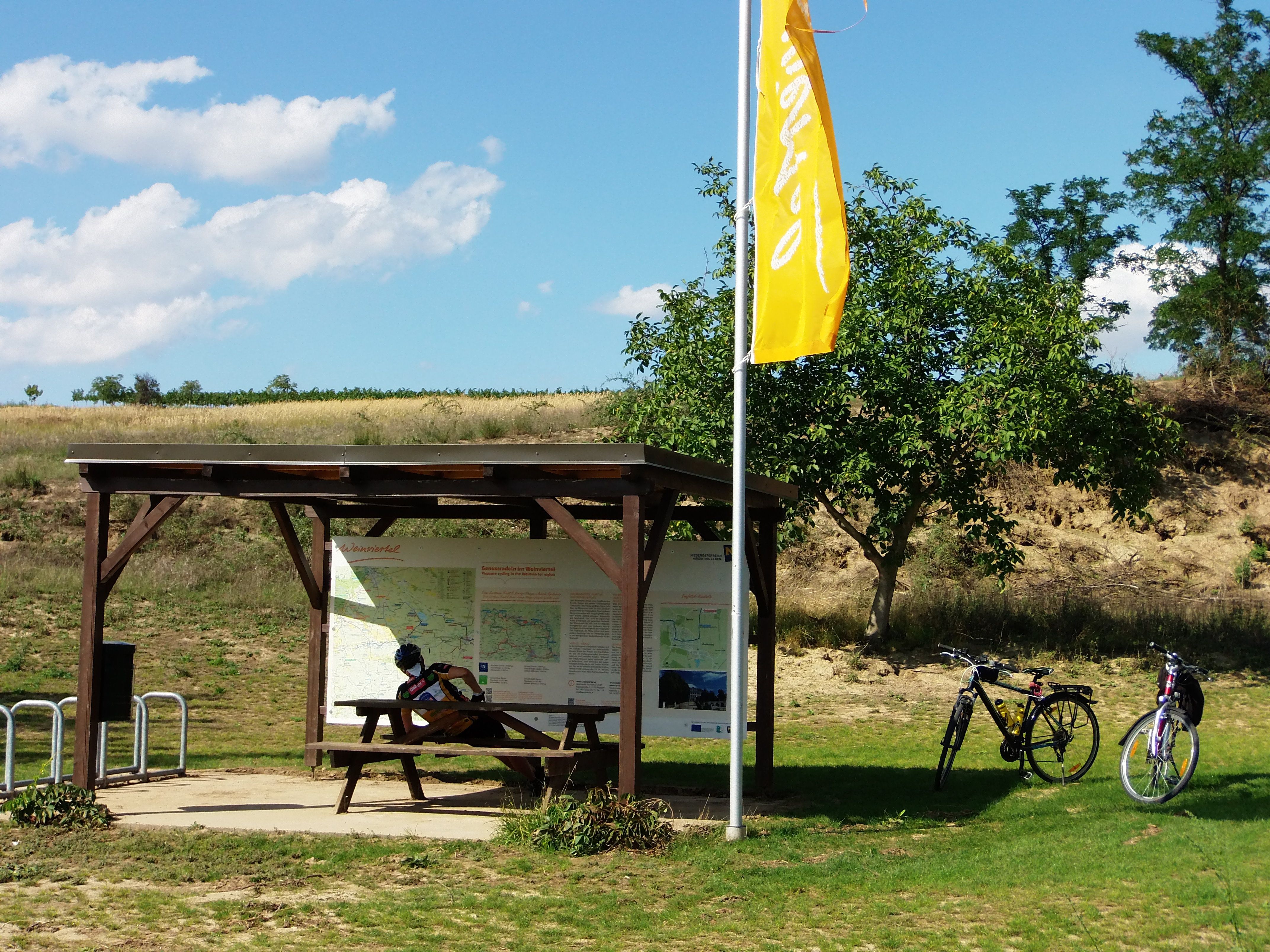 Odpočívadlo pre cyklistov s dreveným stolom, dvoma bicyklami a informačnou tabuľou v obci Weinviertel.
