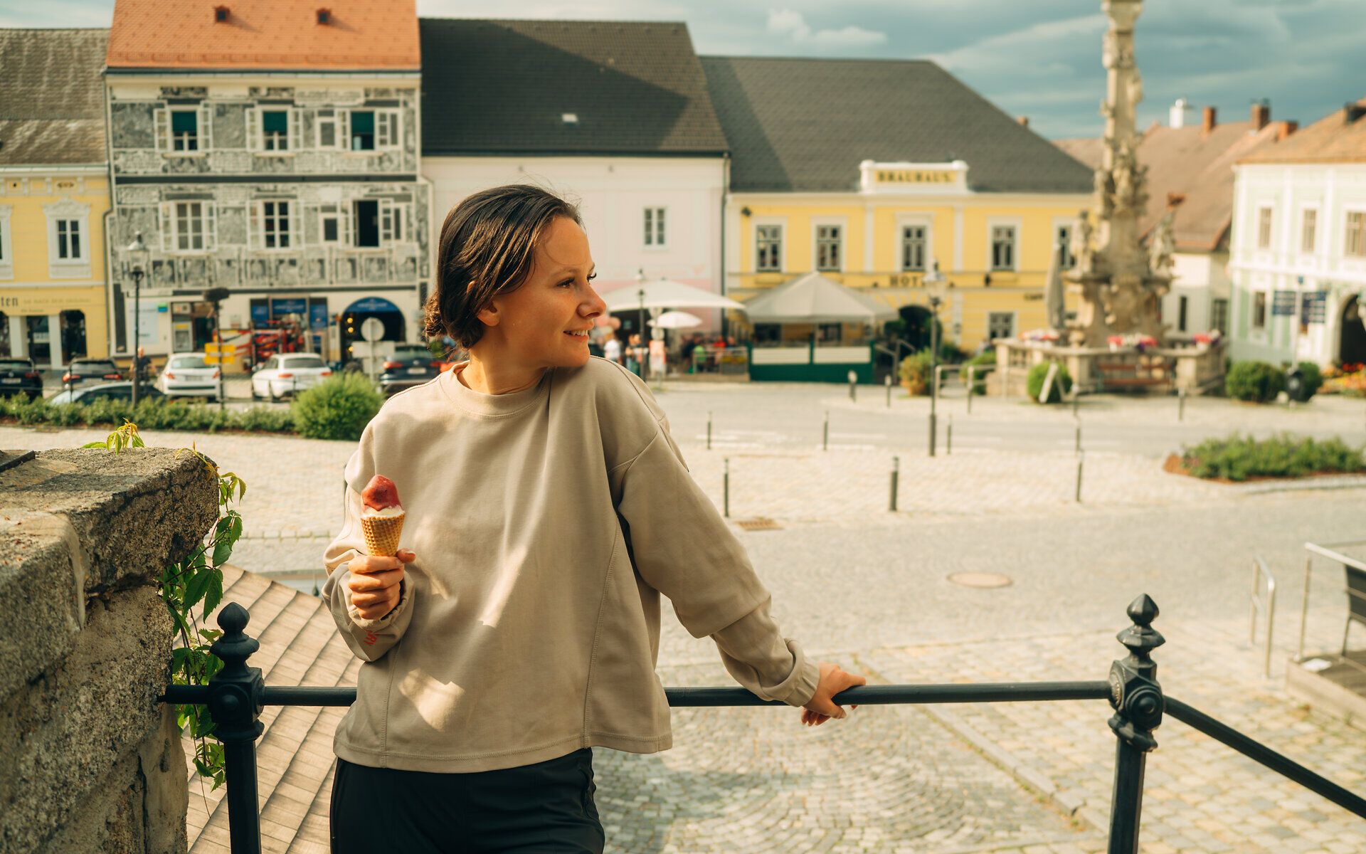 Žena stojí pred zábradlím a pozerá sa na hlavné námestie vo Weitre, v ruke drží zmrzlinu.