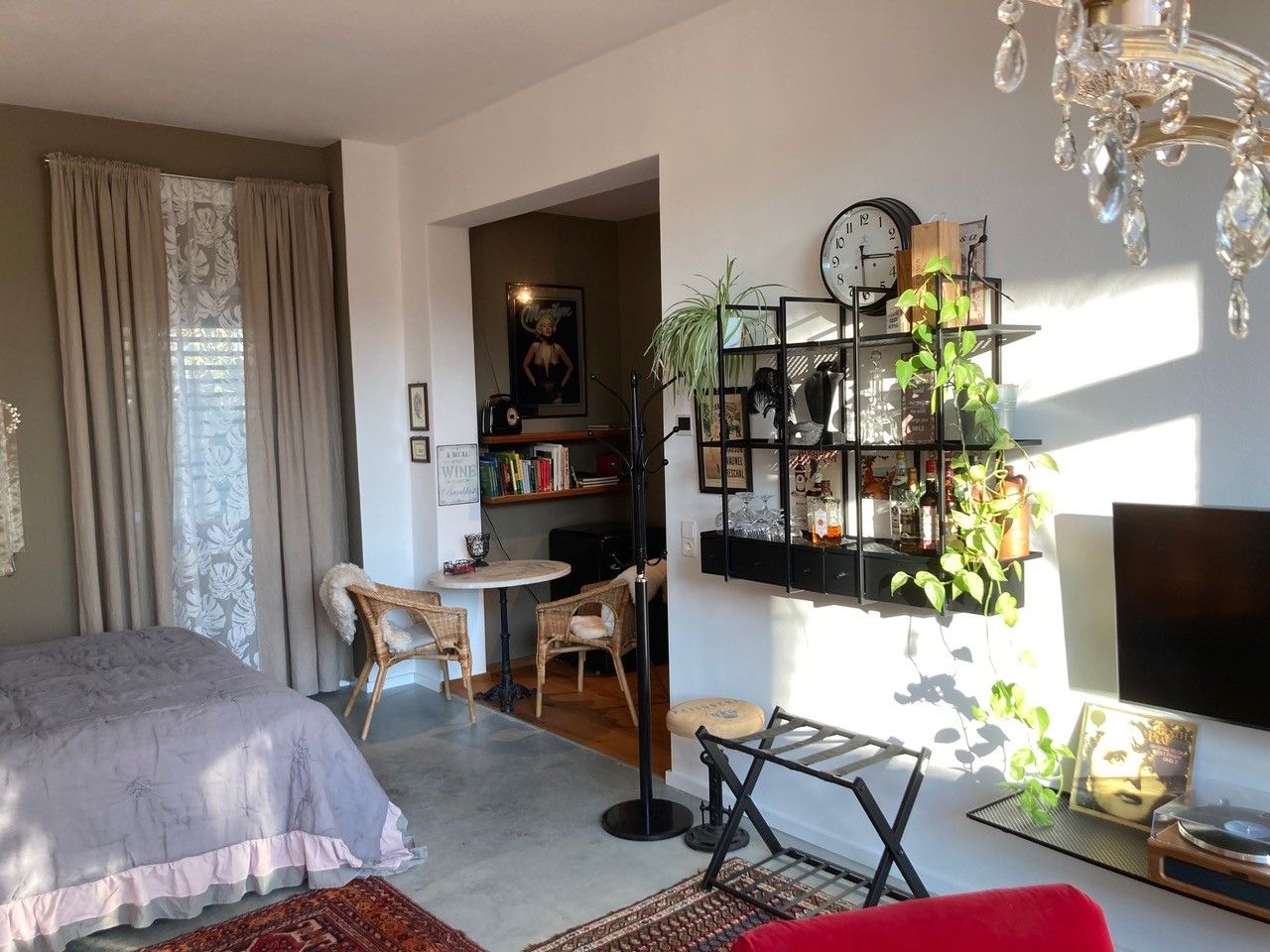 Útulná obývacia izba s posteľou, policou, rastlinami a nástennou dekoráciou.