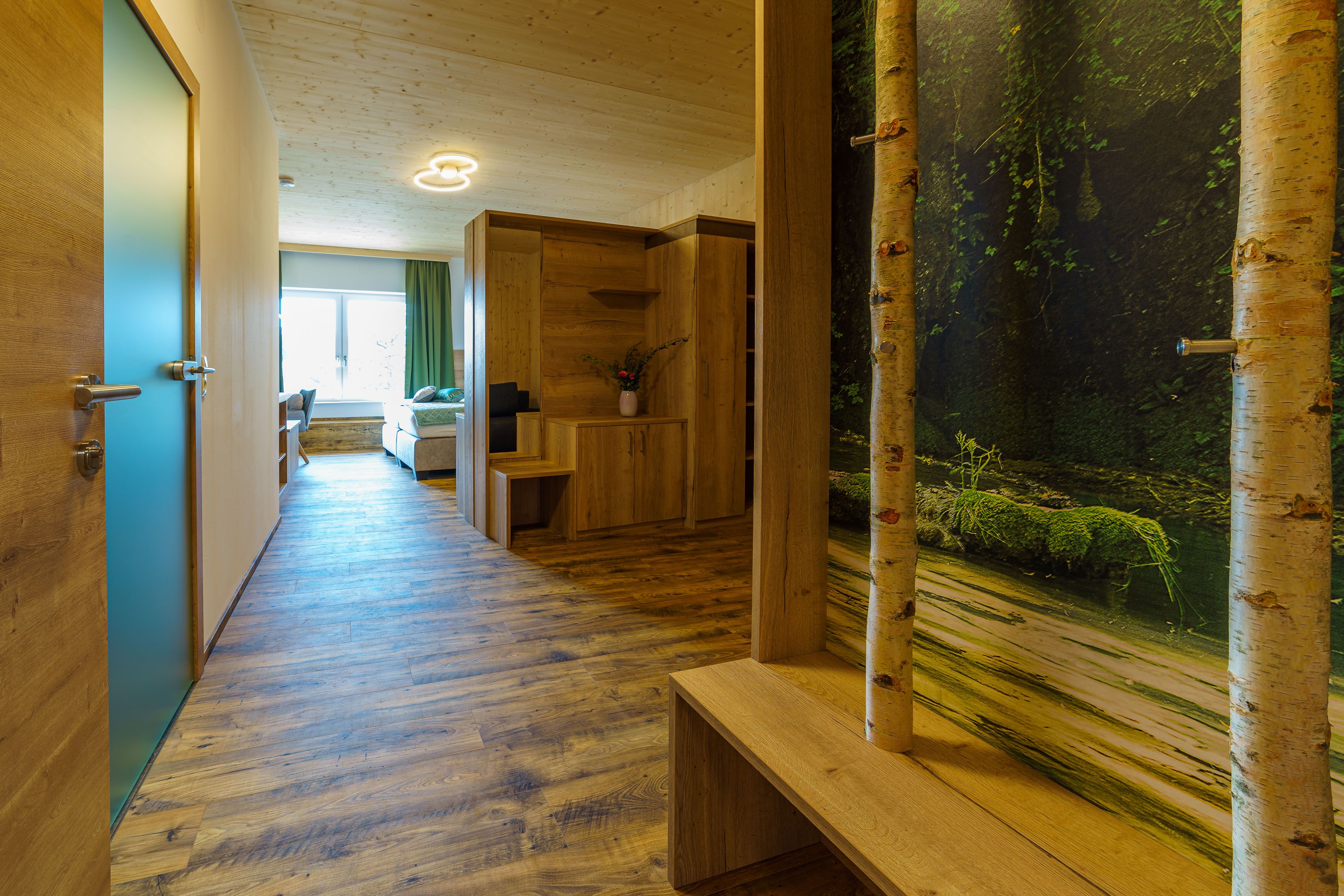 Pohľad do interiéru moderného bytu s drevenou podlahou, dreveným nábytkom a veľkým oknom.