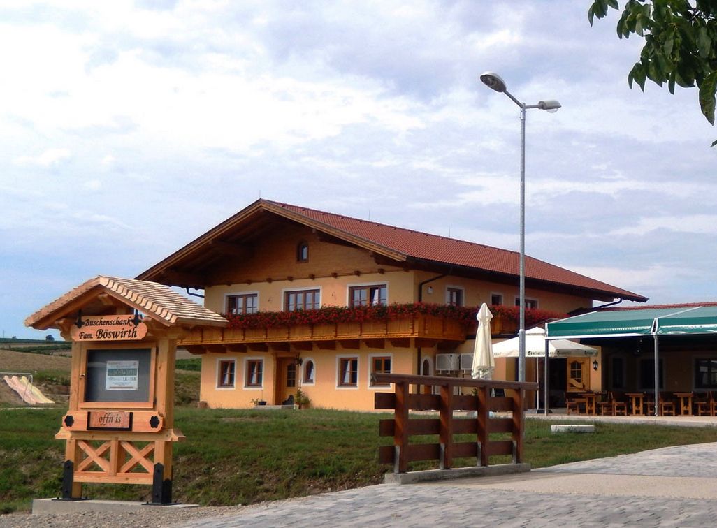 Tradičný hostinec s dreveným balkónom a kvetinovou výzdobou, vedľa nápisu "Vínny šenk Fam. Böswirth".