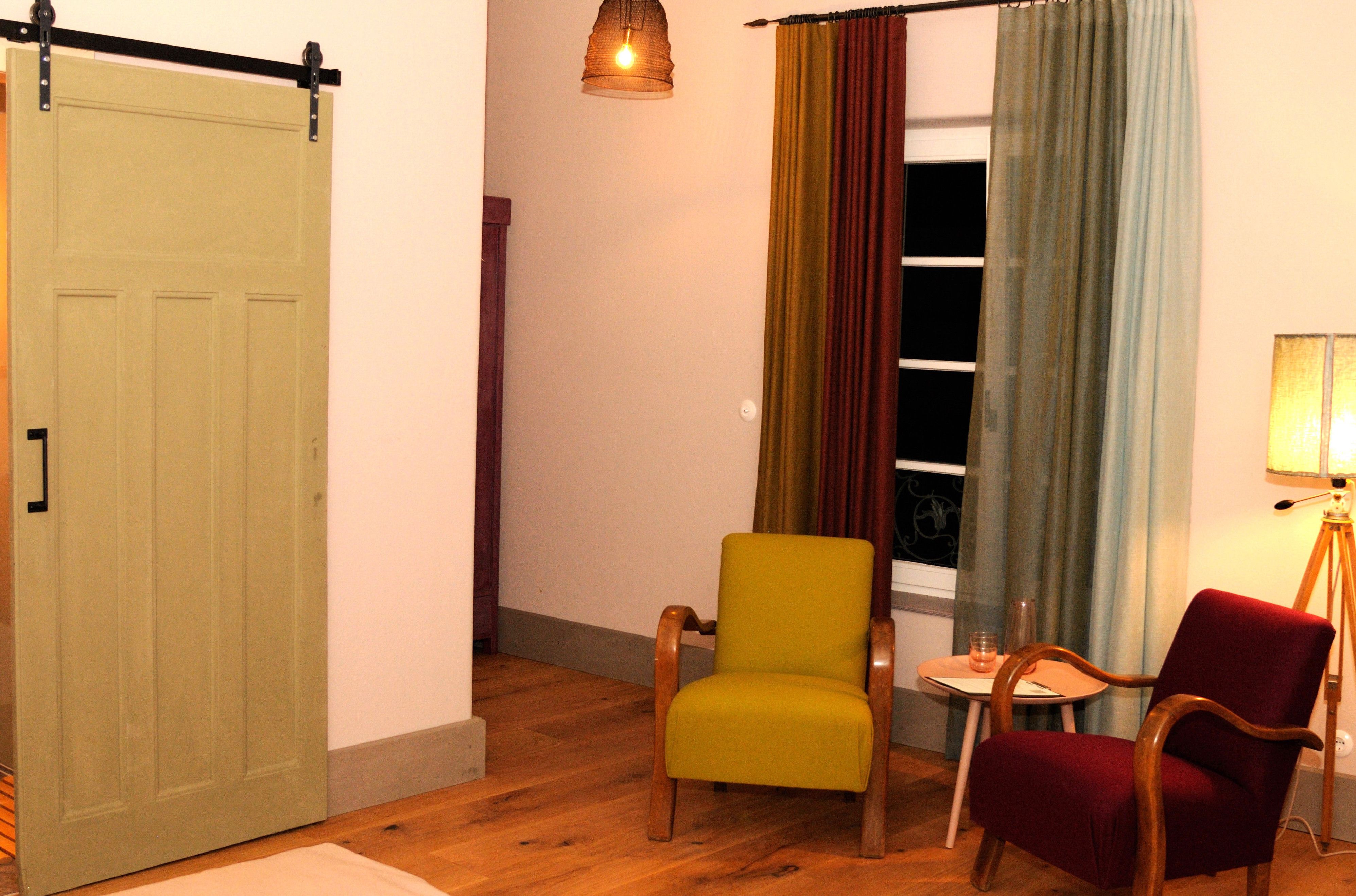 Útulná izba s dvoma kreslami, stolíkom a lampou. Vidno tu aj posuvné dvere a farebné závesy.