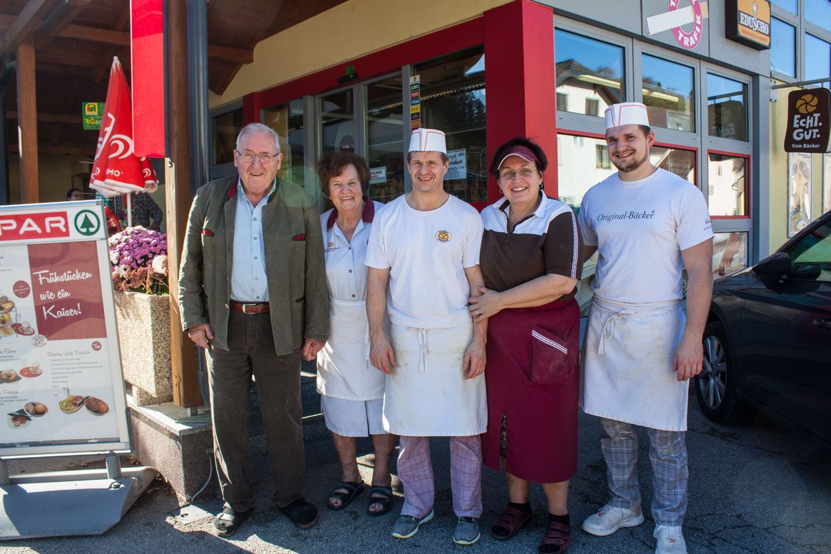 Pred vchodom do obchodu stojí päť ľudí a usmieva sa.