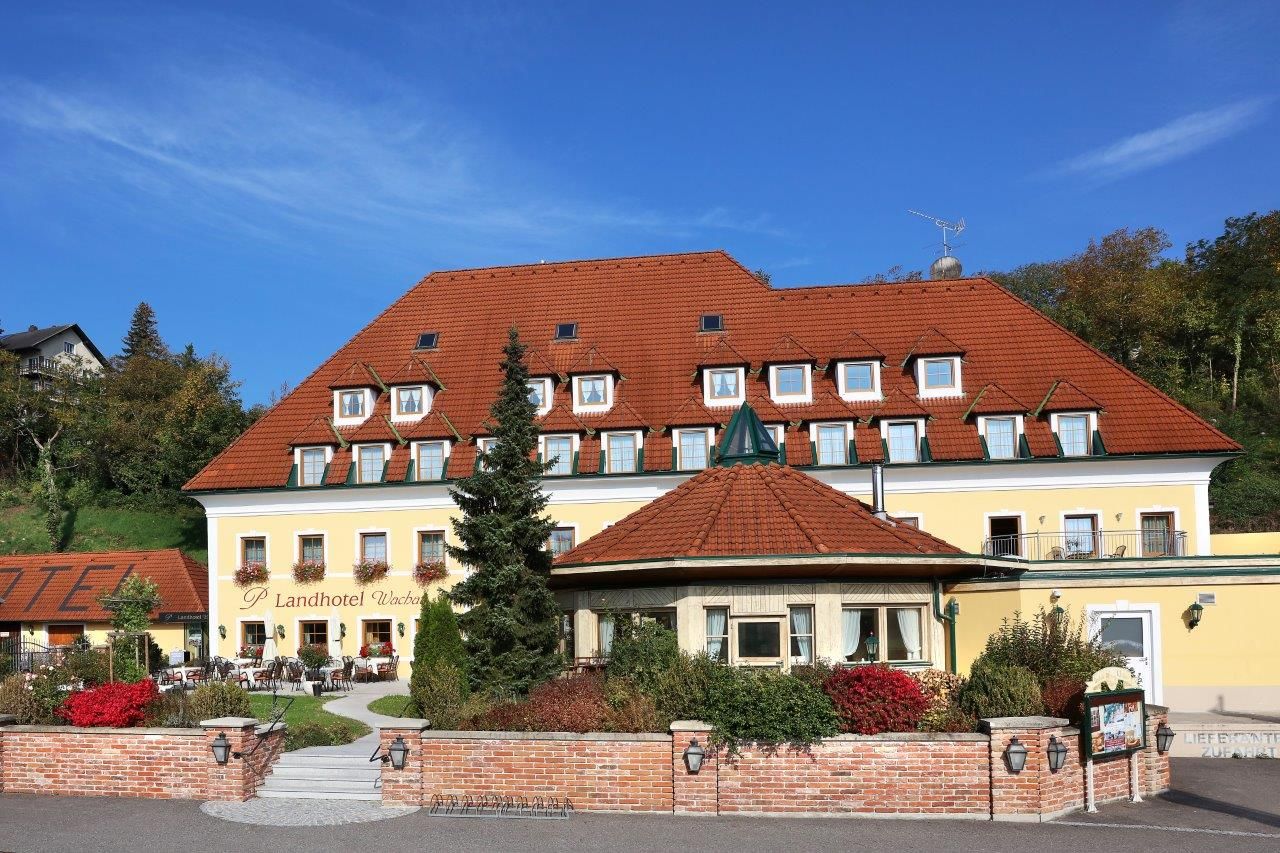 Exteriérový pohľad na žltý vidiecky hotel s červenou strechou a záhradou.