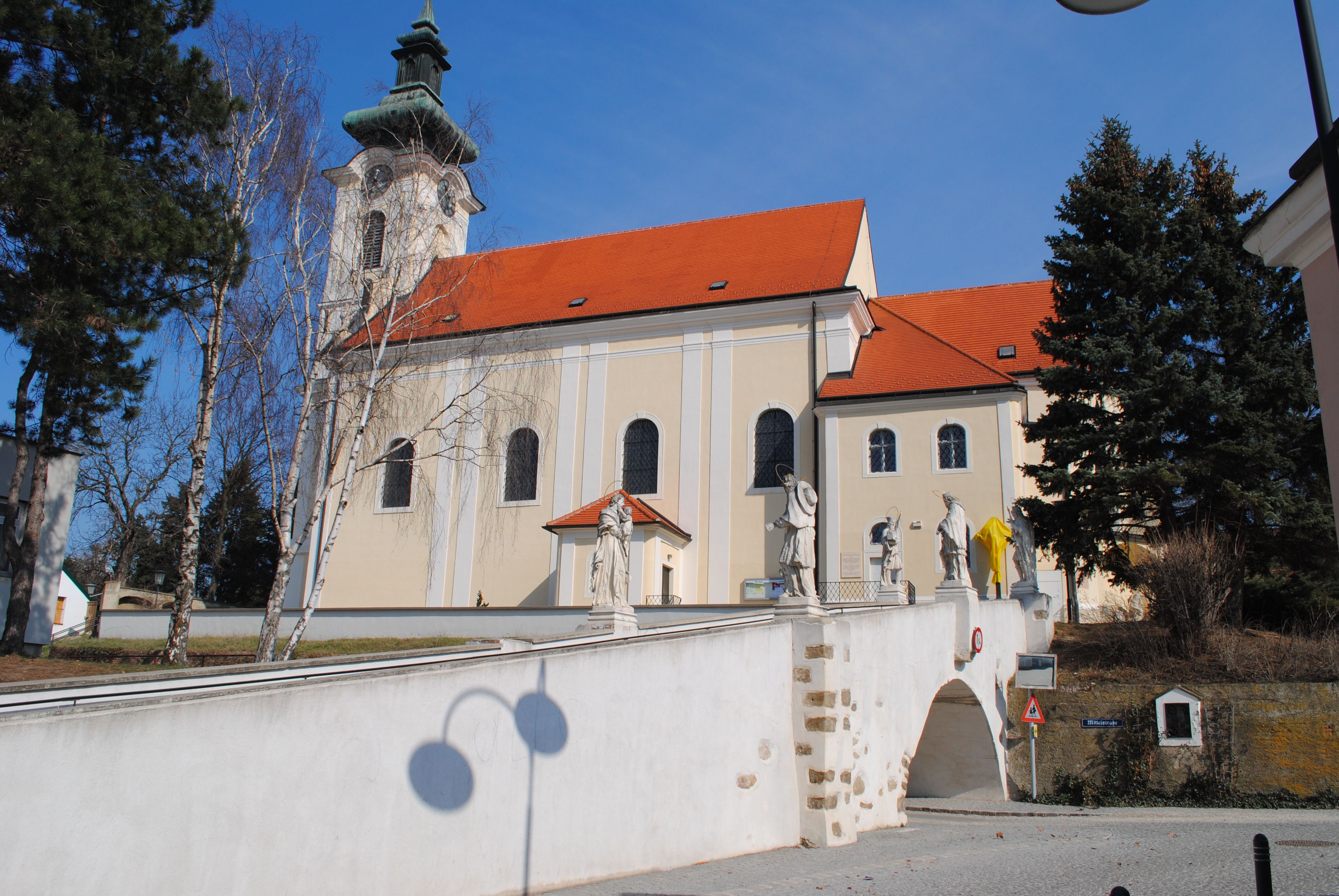 Farský kostol Wolkersdorf so sochami na moste, modrá obloha.