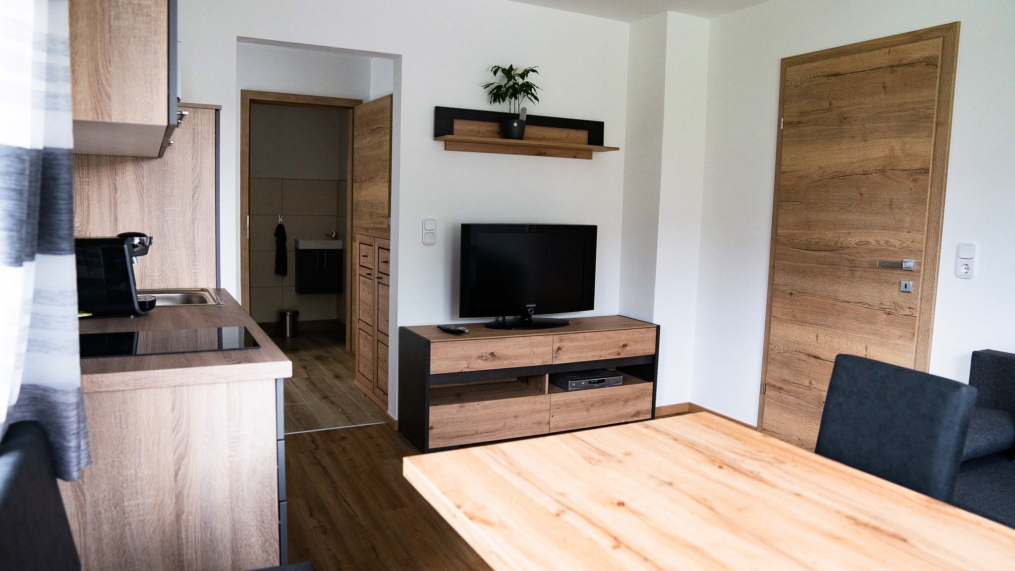 Moderná obývacia izba s dreveným nábytkom, TV a kuchyňou.