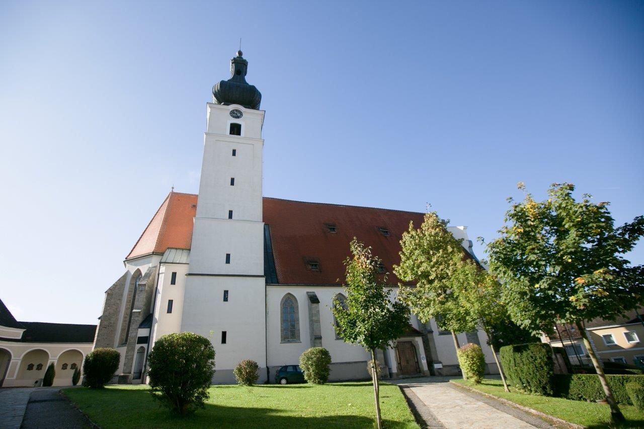 Pútnický kostol s vežou a červenou strechou, obklopený stromami a trávnikom.