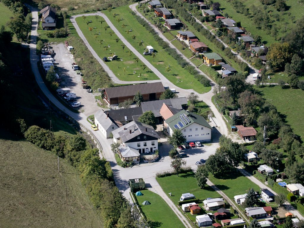 Letecký pohľad na kemp s karavanmi a budovami v zelenej krajine.