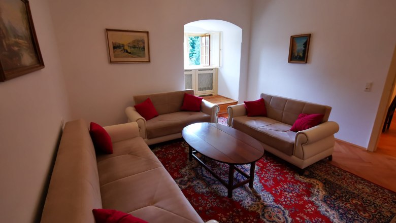 Ob&yacute;vacia izba s tromi pohovkami, červen&yacute;m kobercom a obrazmi na sten&aacute;ch.