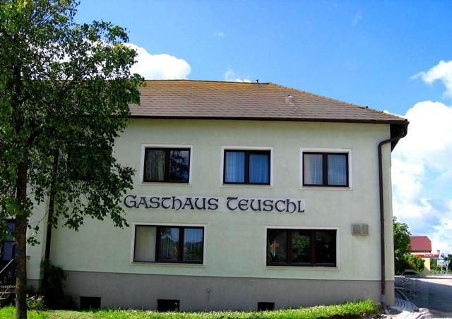 Exteriérový pohľad na hostinec Teuschl so stromami a modrou oblohou.