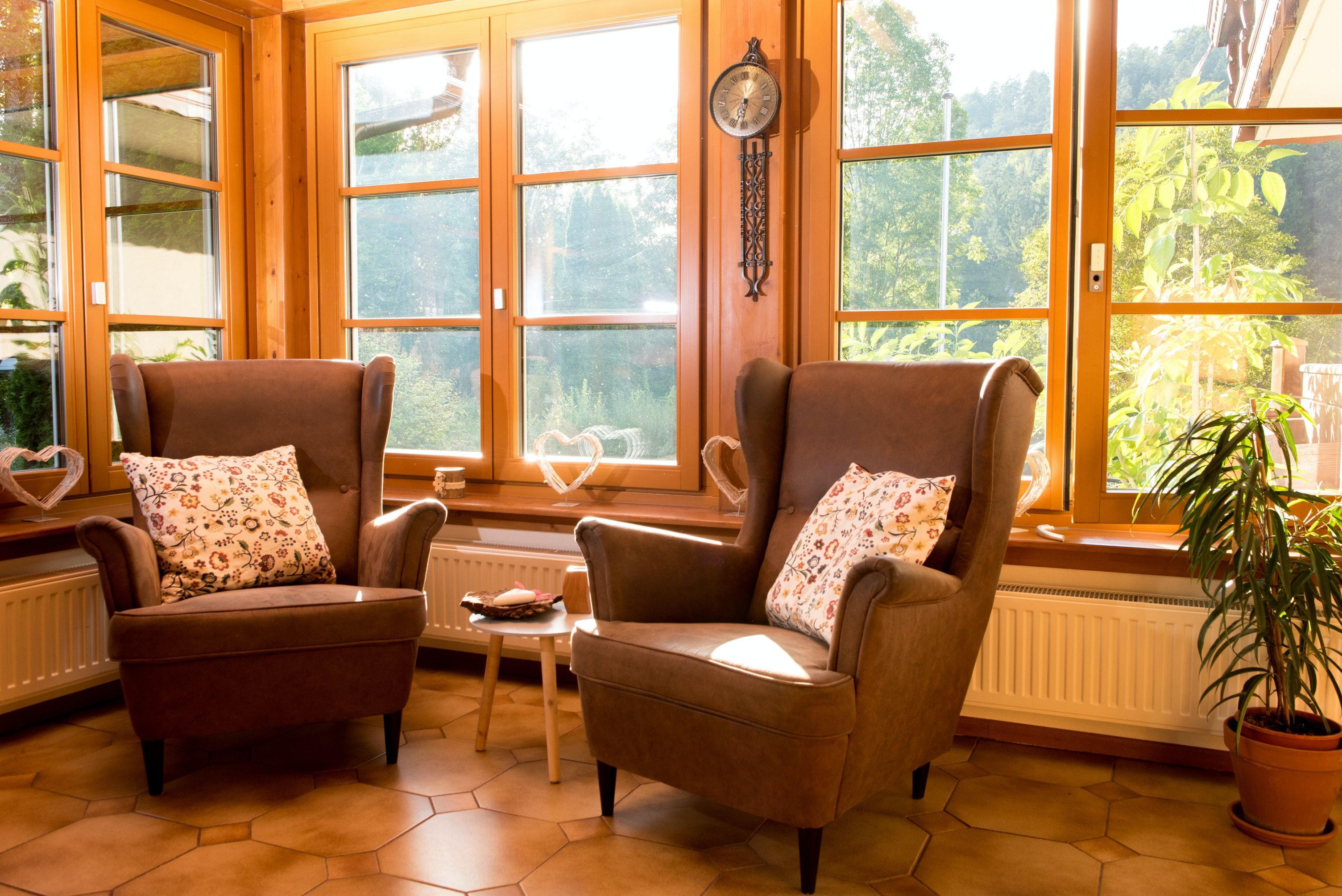 Dve hnedé kreslá so vzorovanými vankúšmi pred veľkými oknami v slnečnej miestnosti.