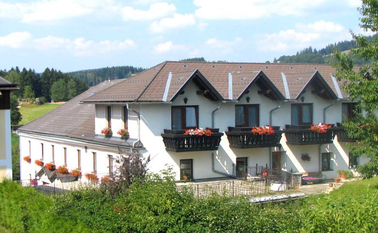 Veľká biela budova s hnedými strechami a balkónmi s kvetmi.