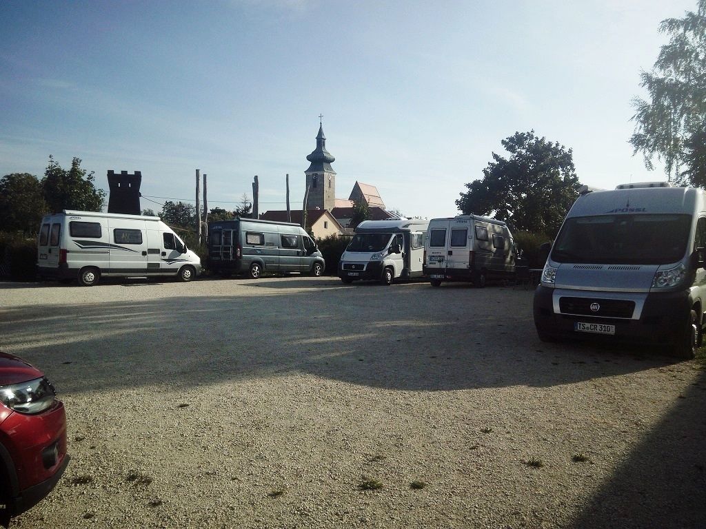 Kemp pre karavany s niekoľkými zaparkovanými karavanmi a kostolom v pozadí.