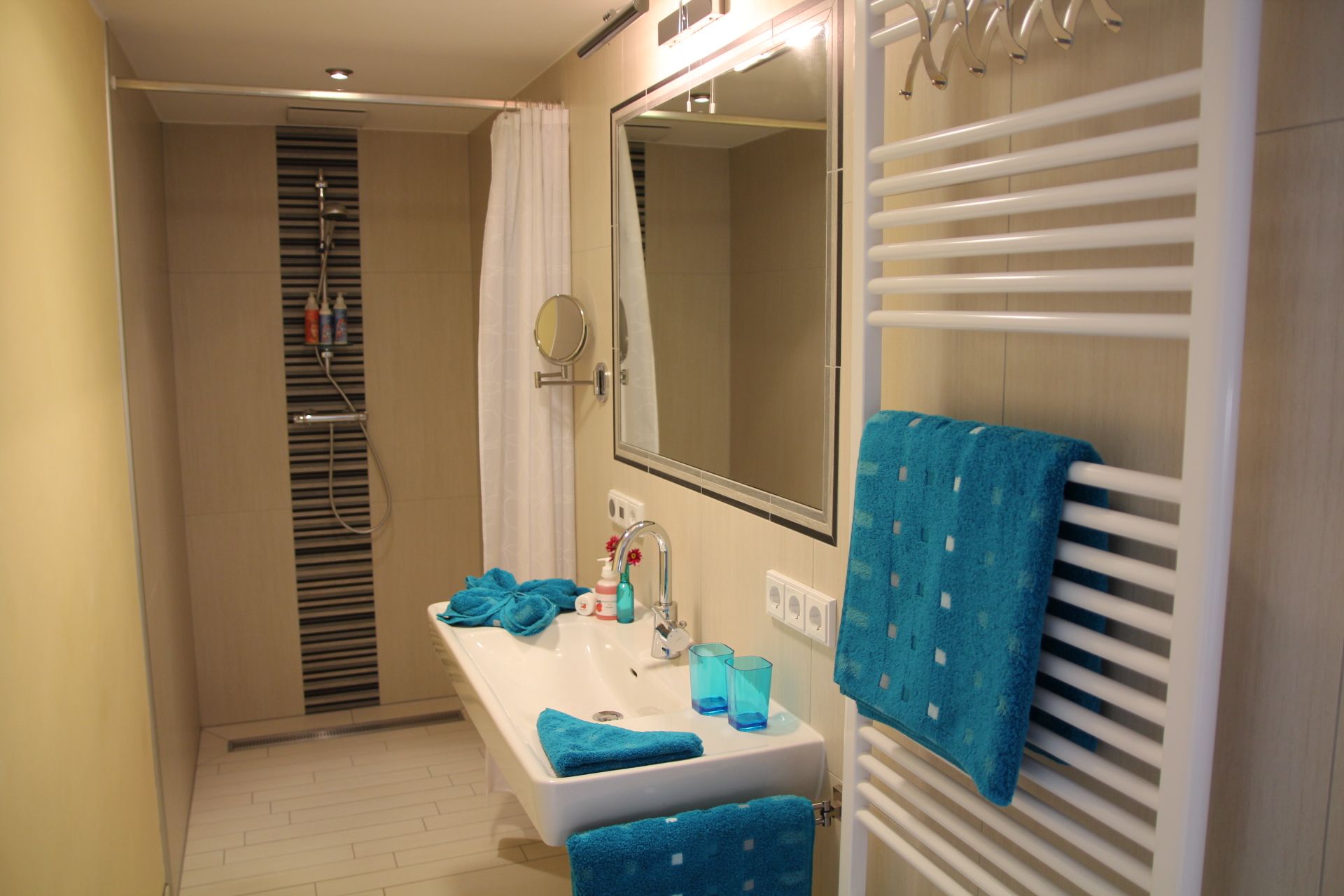 Moderná kúpeľňa so sprchovacím kútom, umývadlom a modrými uterákmi.